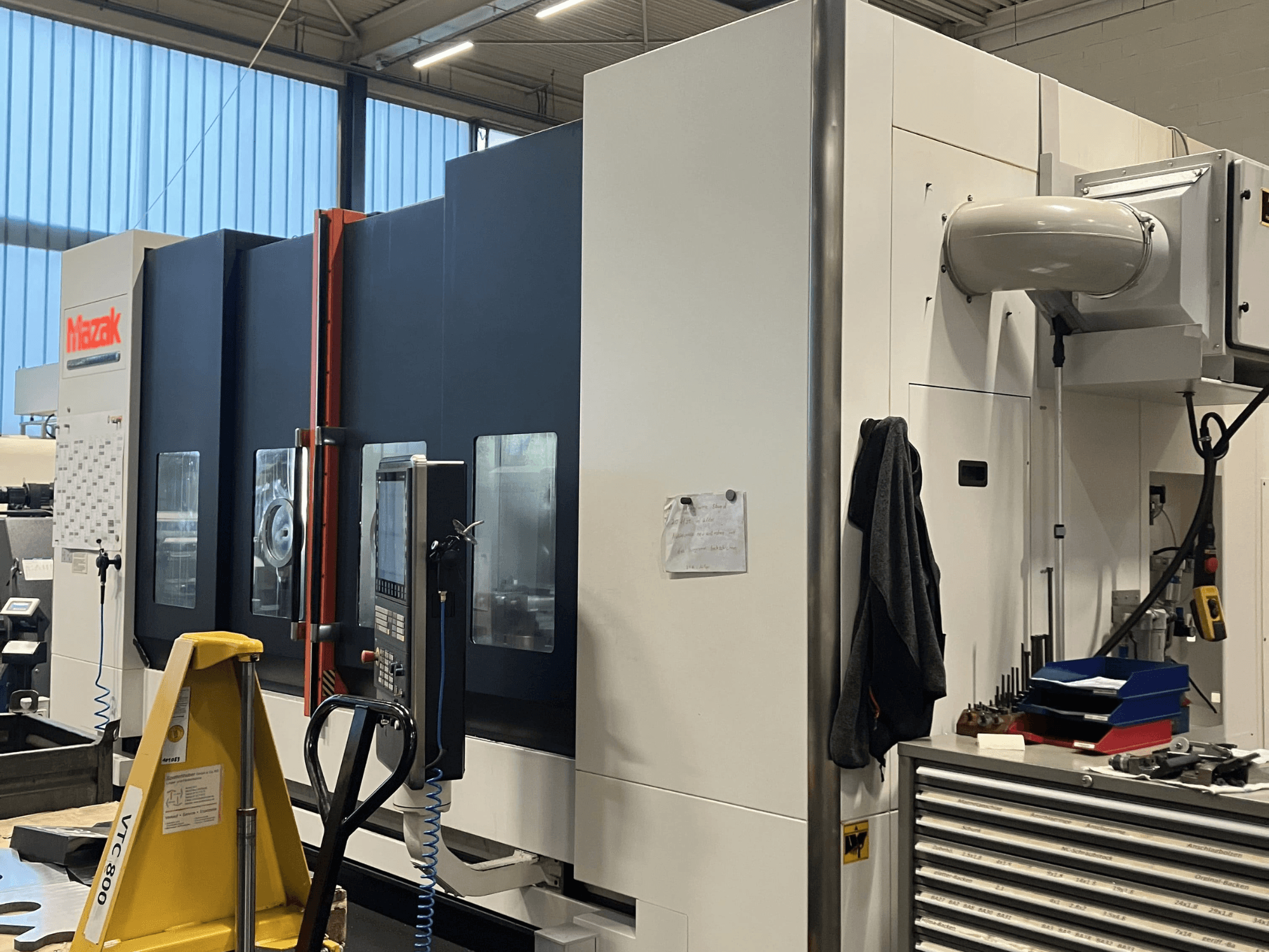 Mazak CNC-maskin sedd från sidan, som visar kontrollpanelen och säkerhetsfunktionerna i en verkstadsmiljö.