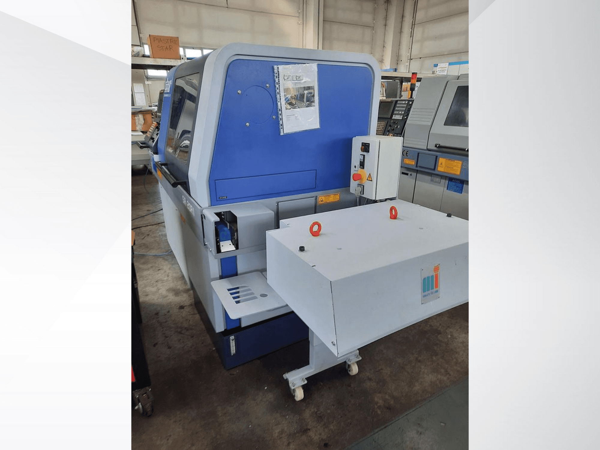 Blå industrimaskin med ett vitt transportband, som visar kontrollpanelen och tillhörande säkerhetsfunktioner, vy från sidan.