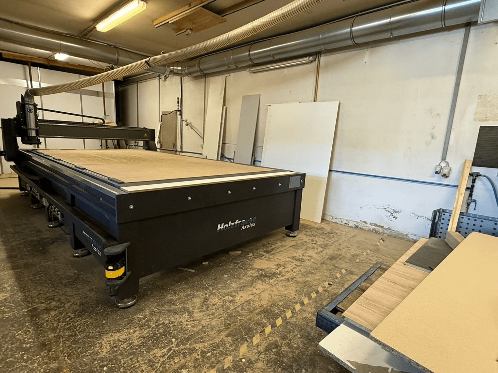 Holz-Her Axos 5 CNC-fräs i verkstad, framifrån med arbetsbord, dammutsugningssystem och träpaneler i närheten.