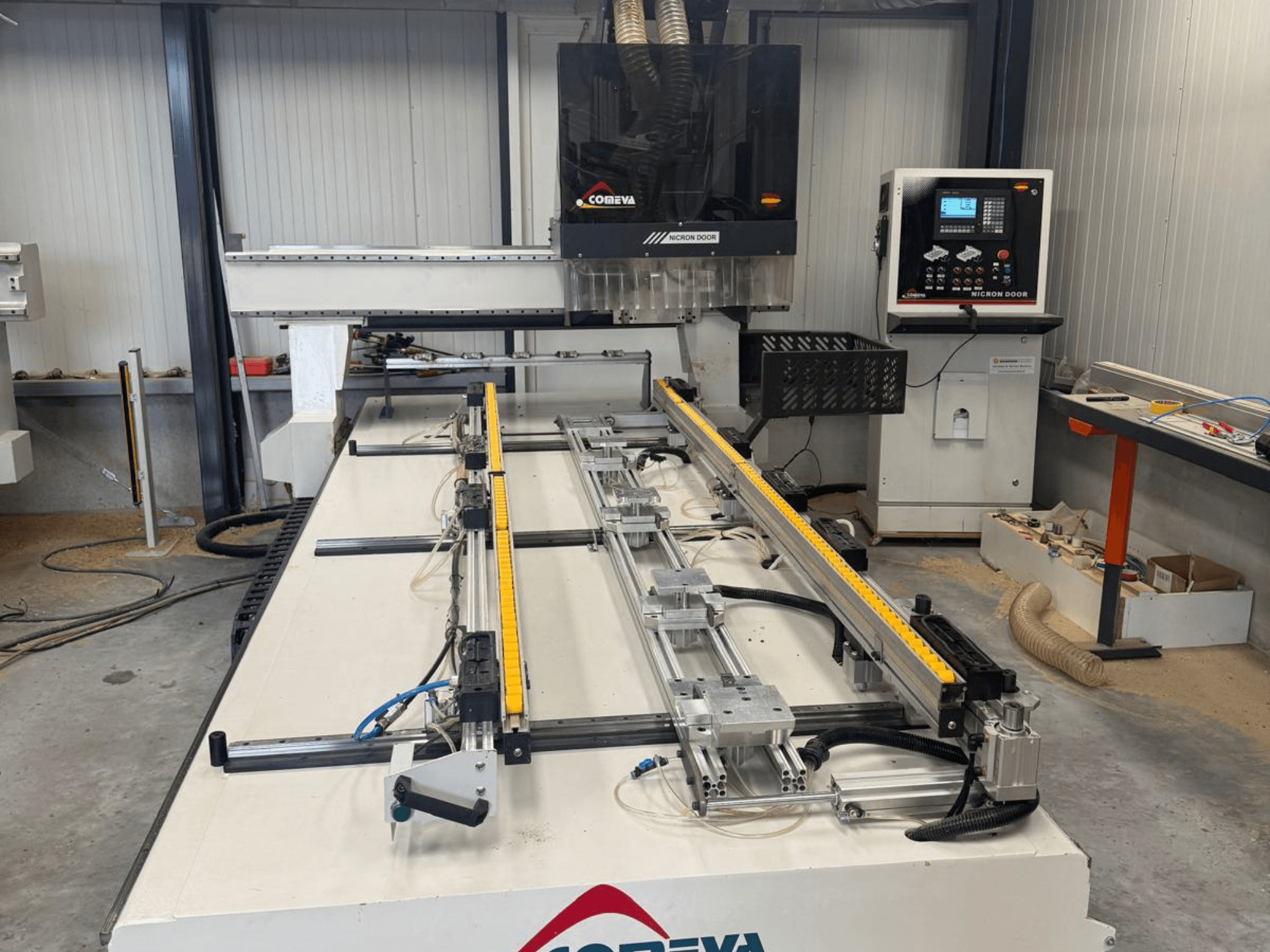 CNC-bearbetningscenter för trä COMEVA MEX V 2100x3260, framifrån sett, med arbetsstation, kontrollpanel och styrskenor.