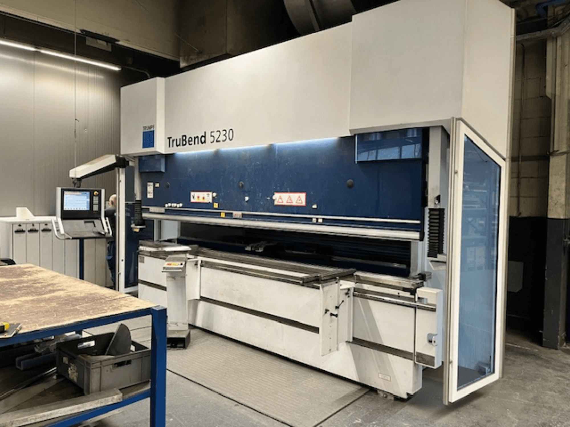 TruBend 5230 bockningsmaskin i industriell miljö; framifrån med kontrollpanel, säkerhetsfunktioner och arbetsbord.