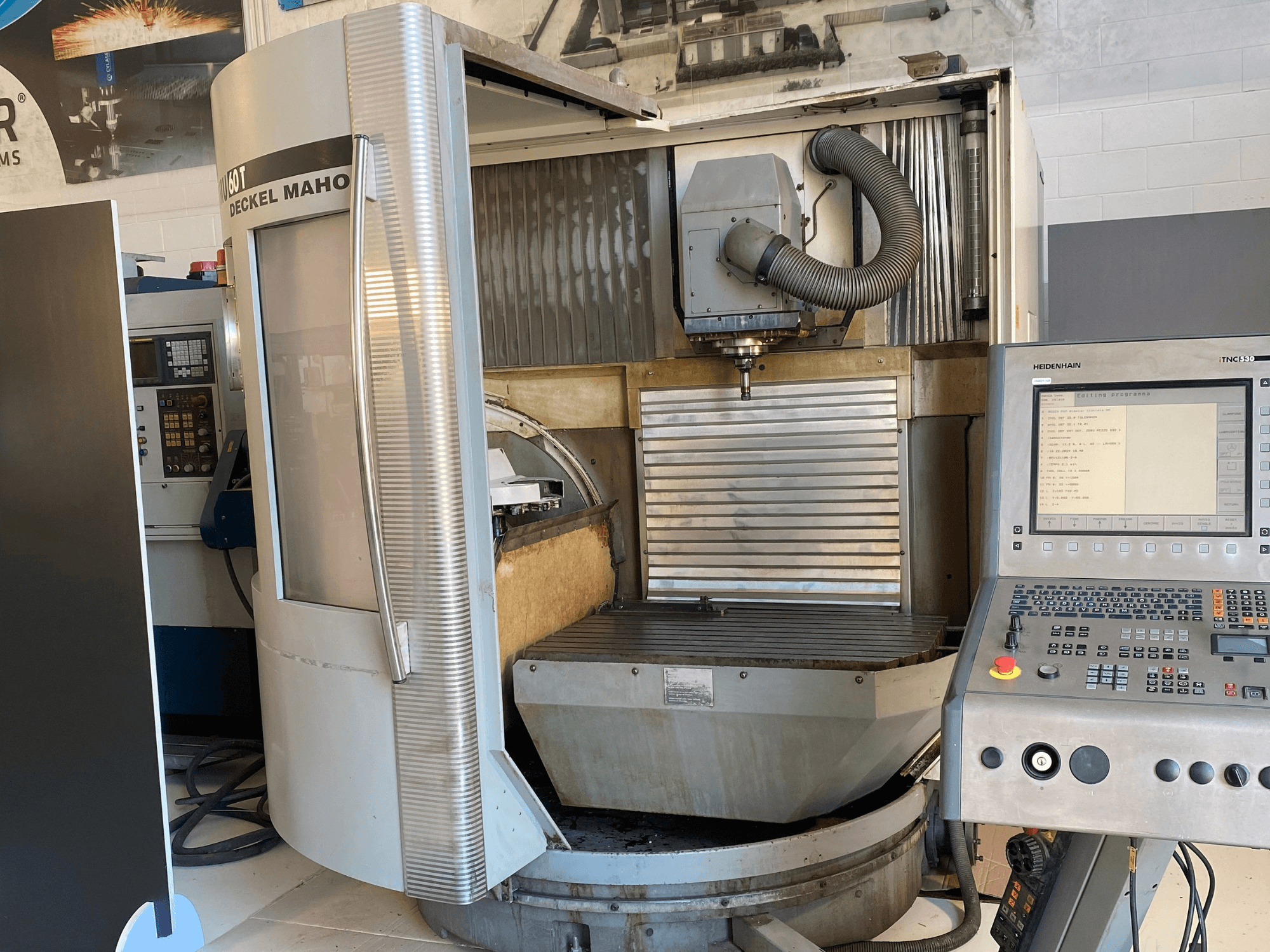 Frontvy av en DECKEL MAHO DMU 60T fräsmaskin med kontrollpanel, spindel och fräsbord synliga.