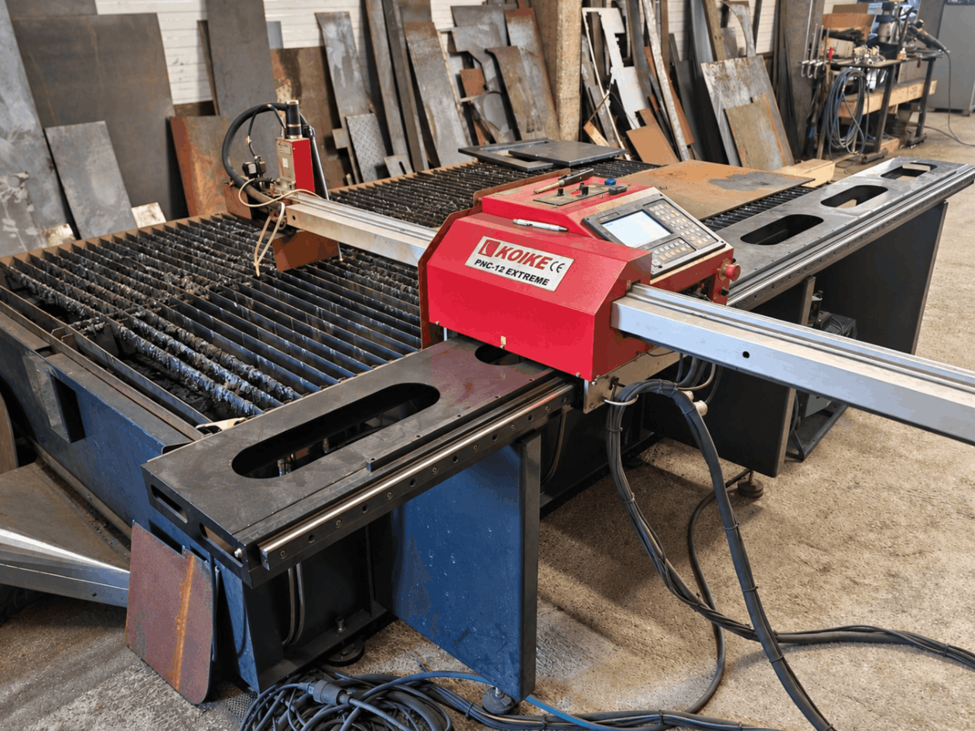 Framifrån sett: plasmaskärmaskinen KOIKE PNC-12 Extreme med metallskärbord, kontrollpanel och kablar.