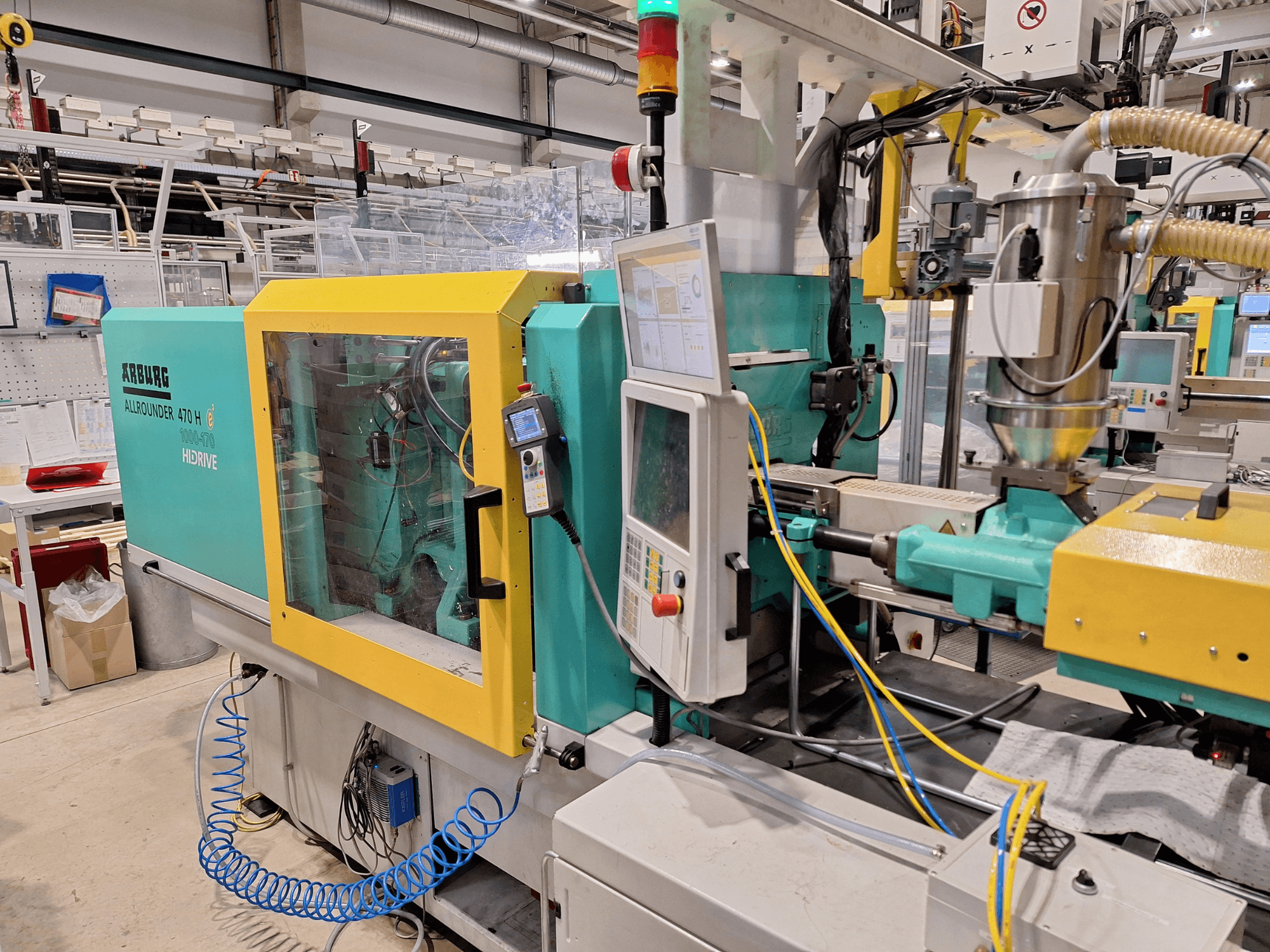 Arburg 470 H 1000-170 hydraulisk formsprutningsmaskin, sidovy som visar kontrollpanelen och matningssystemet.