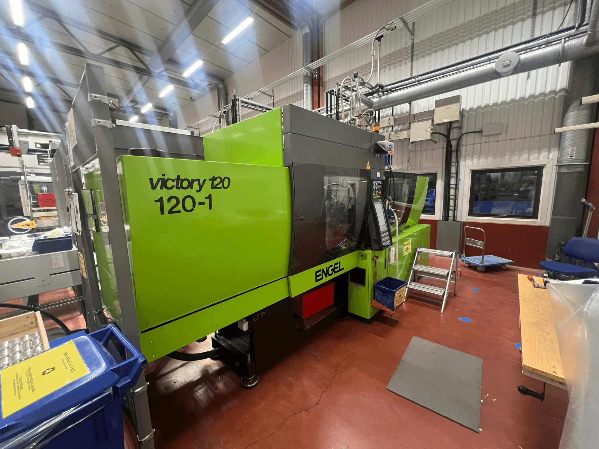 Grön ENGEL Victory 120-1 formsprutningsmaskin, framifrån, med kontrollpanel och steg, i en industrimiljö.