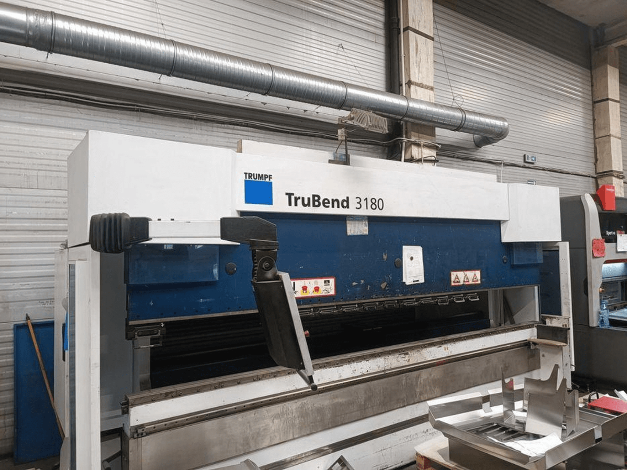 Trumpf TruBend 3180 bockningsmaskin i en verkstad, sidovy som visar kontrollpanelen och metallstycken på bordet.