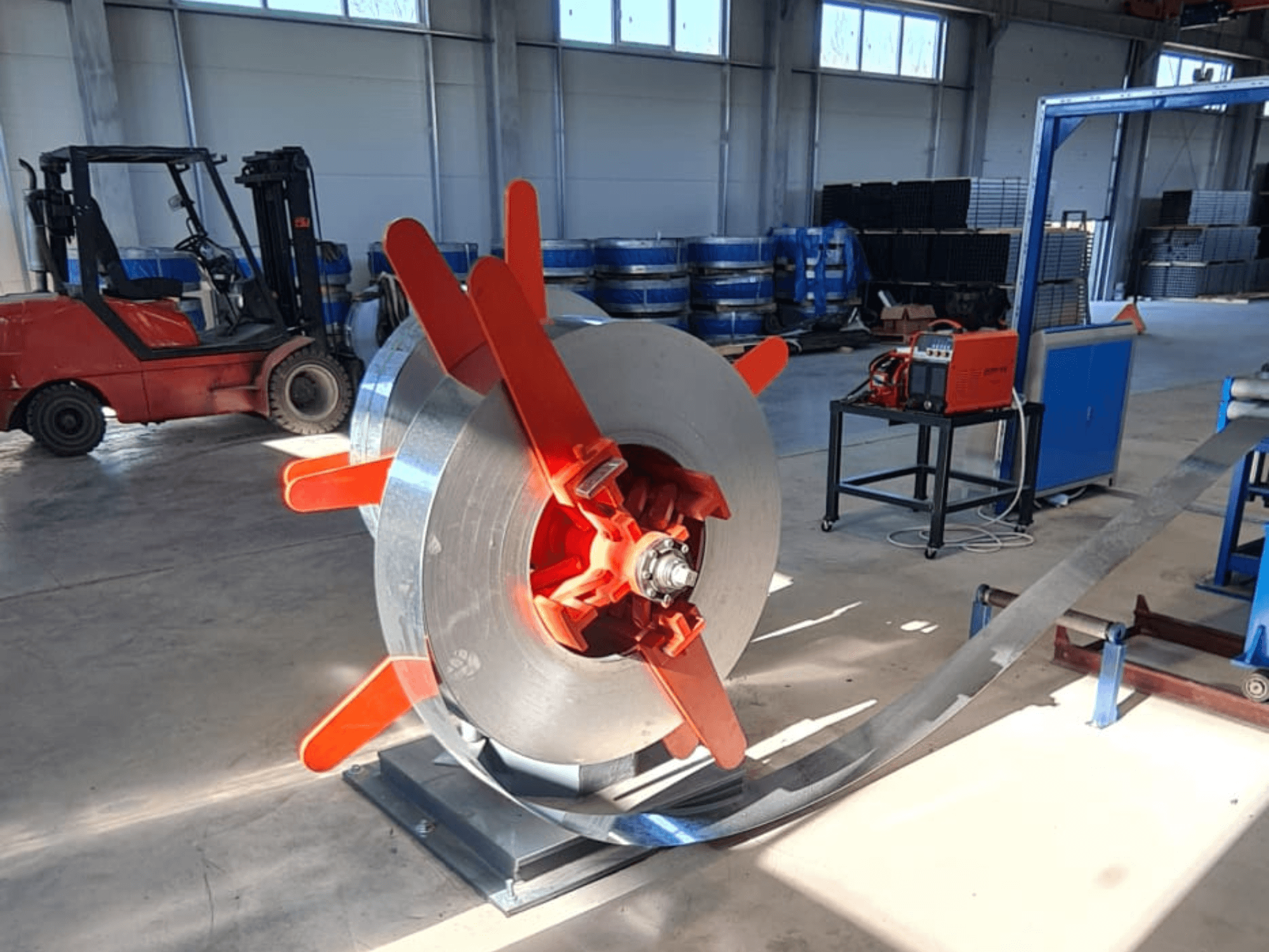 Metallspole med röda handtag på ett stativ, sett från en vinkel. Industriell bakgrund med maskiner och en gaffeltruck.