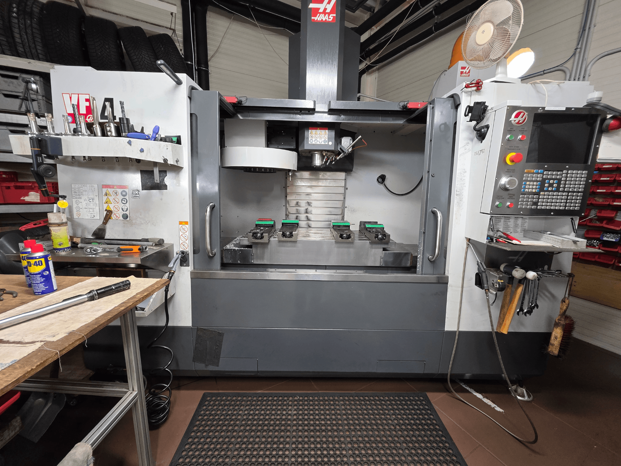 Haas VF-4 CNC-fräs framifrån i en verkstad, med verktyg, ett datorgränssnitt och två arbetsstycken på bordet.