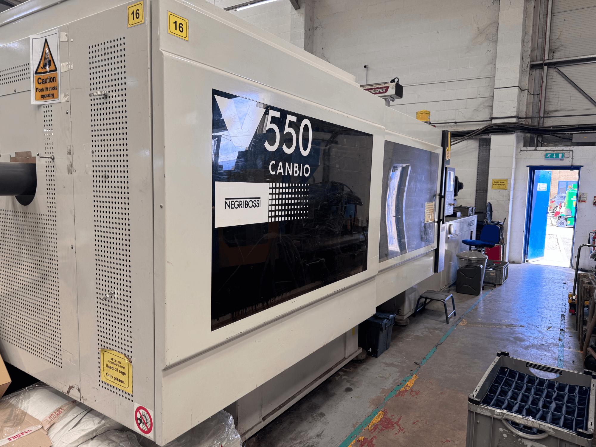 Hydraulisk formsprutningsmaskin av typen Negri Bossi 5500H-4250, framifrån sett med kontrollpanelen och varningsskyltarna.