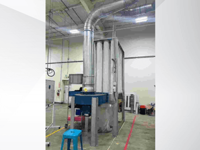 Stort industriellt ventilationssystem, sett framifrån, med blanka metallkanaler och blå bas, placerat i en rymlig lagerlokal.