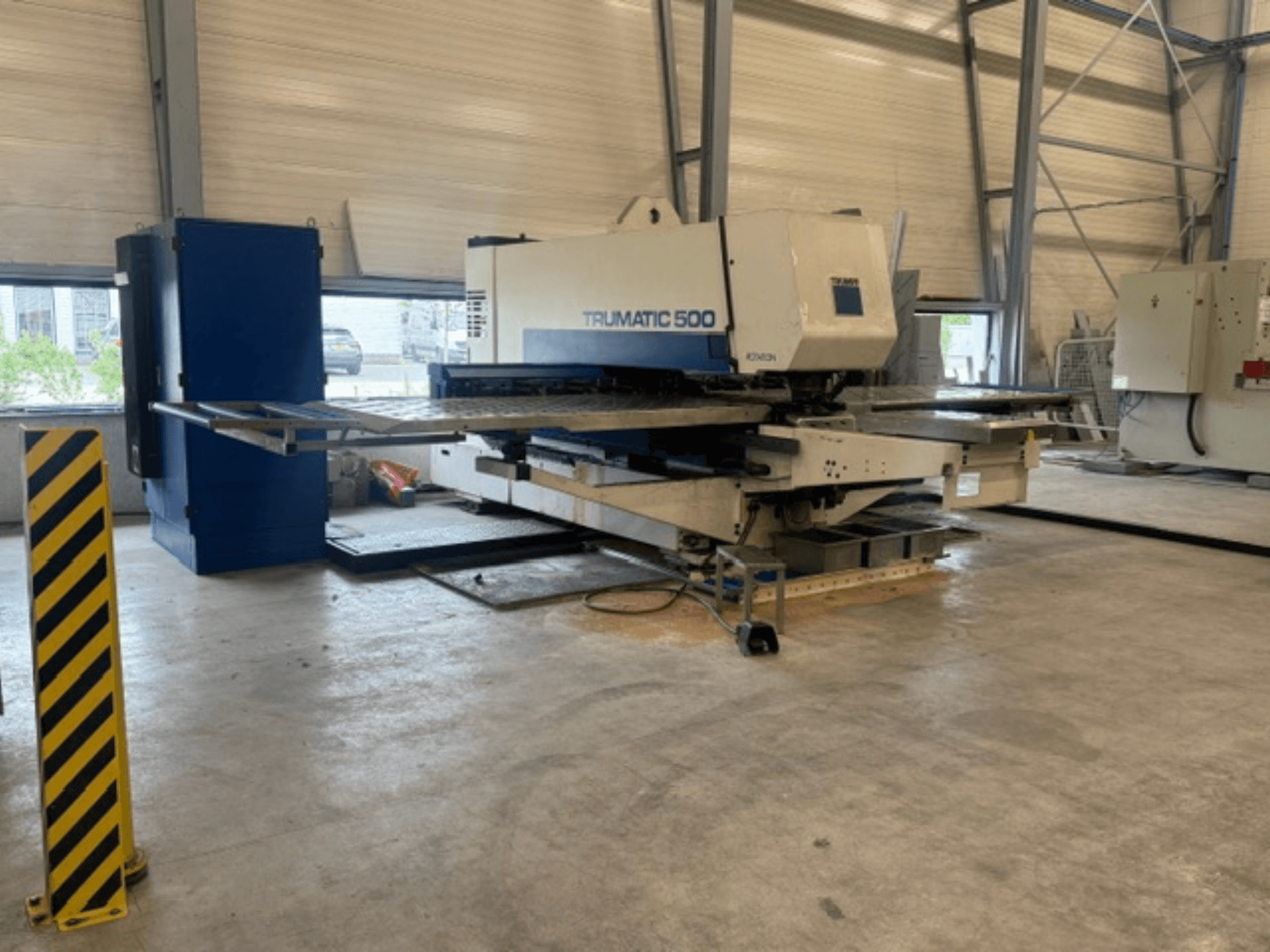 CNC-stansmaskin TRUMPF Trumatic 500 i en verkstad, sidovy som visar maskinen och säkerhetsstolpen med gula ränder.