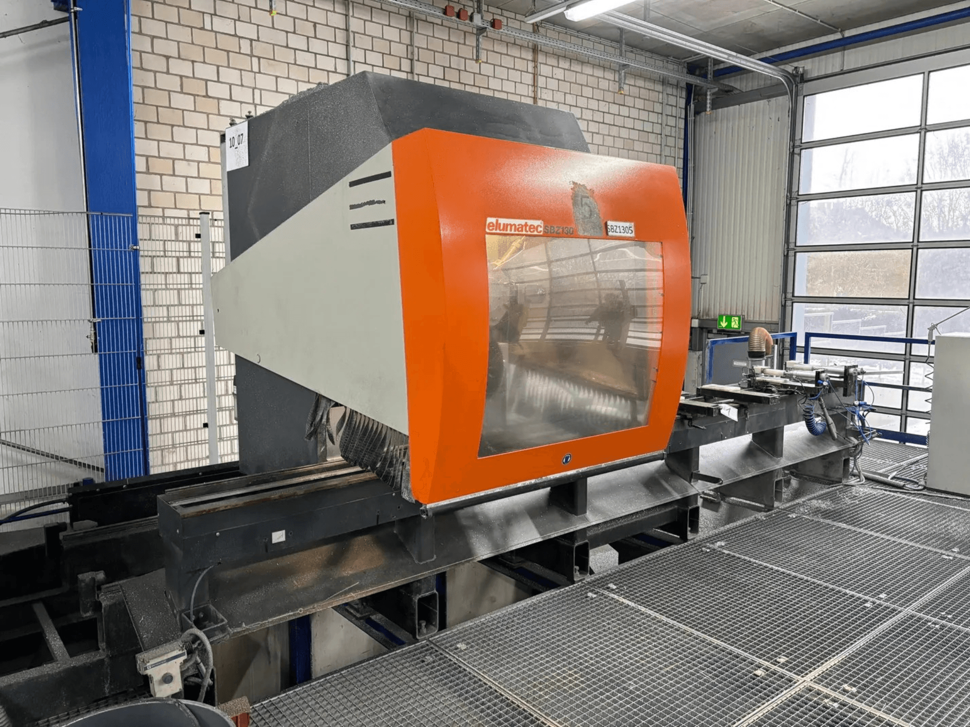 Elumatec SBZ 130 vertikal fleroperationsmaskin, framifrån, med orange och grått hölje med transparent panel.