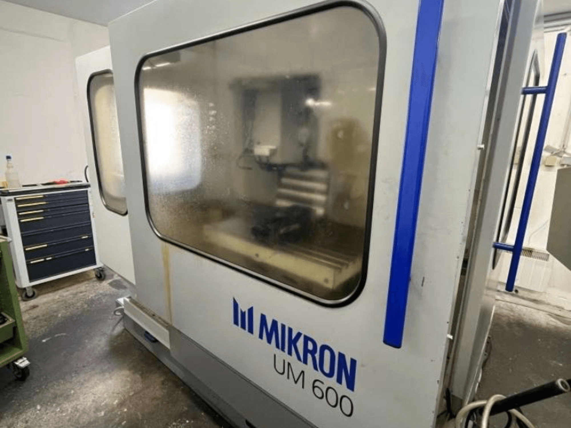 MIKRON UM 600 TNC 410/426 universalbearbetningscenter, vy från sidan, med immigt glas och synlig verktygsförvaring i närheten.