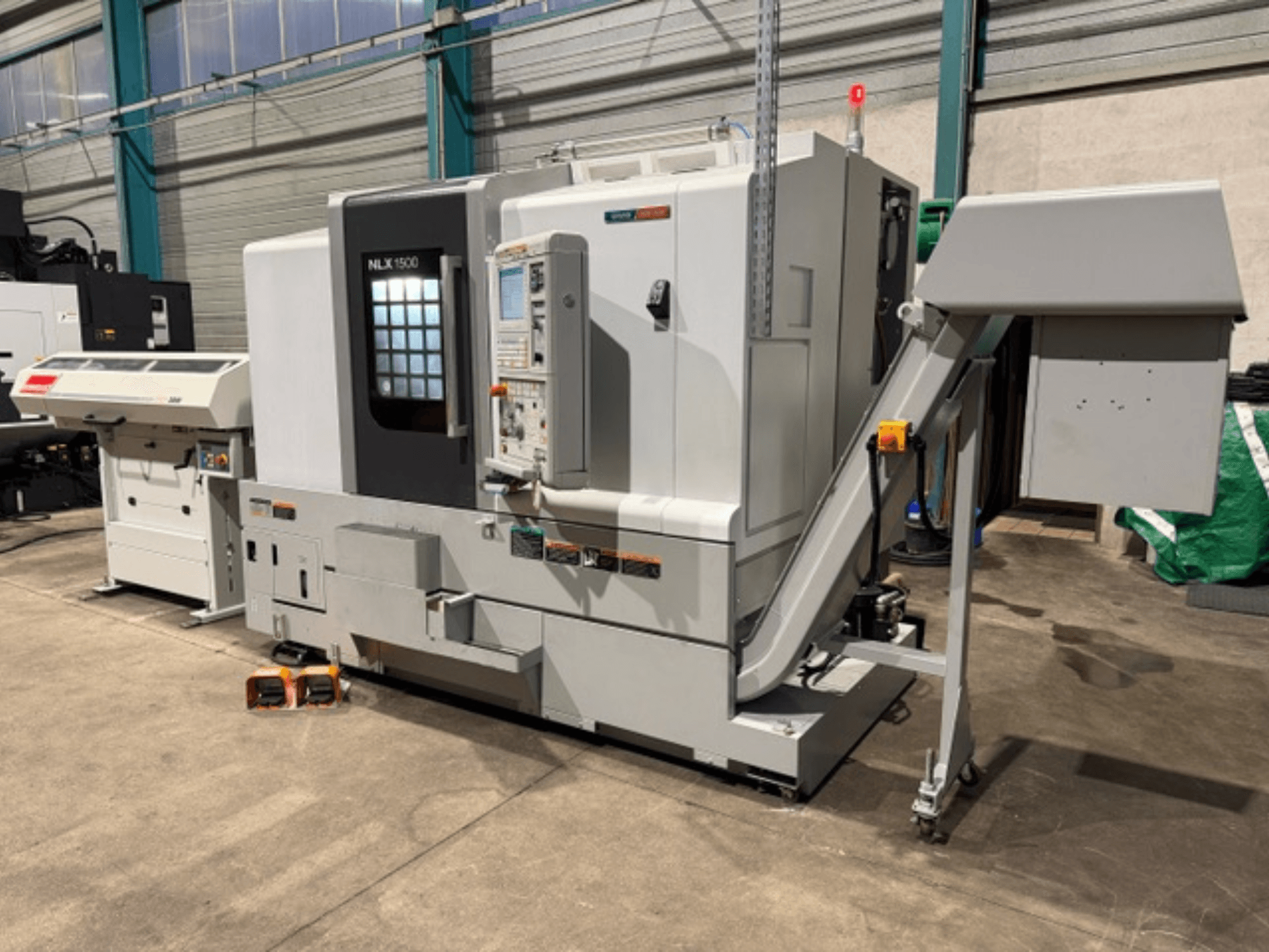 NLK 1500 CNC-maskin, framifrån, med kontrollpanel och tillbehörsbehållare på sidan, vilande på betonggolv.
