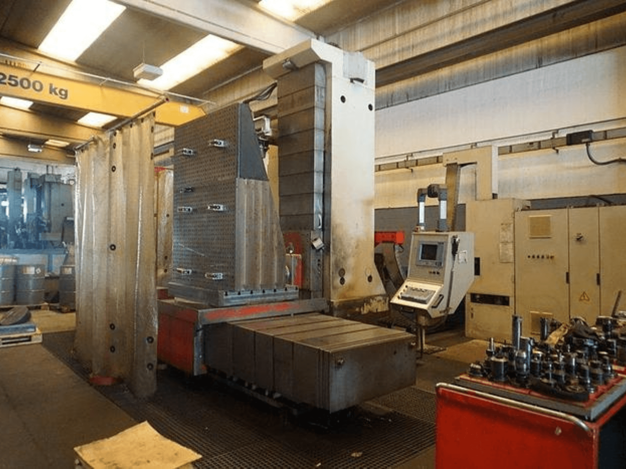 Industriell fräsmaskin med pekskärmsstyrning och stort arbetsbord, sedd framifrån i en verkstadsmiljö.