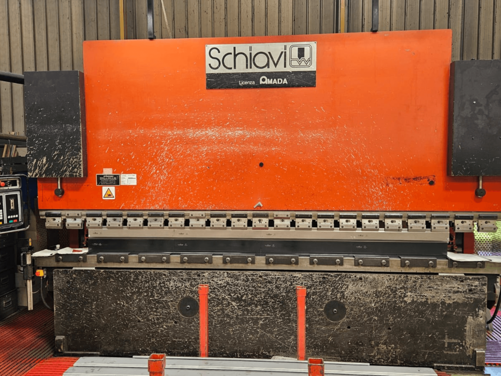 Schiavi Amada metallbockningsmaskin, framifrån, med orange kaross, kontrollpanel till vänster och flera bockningsverktyg synliga.