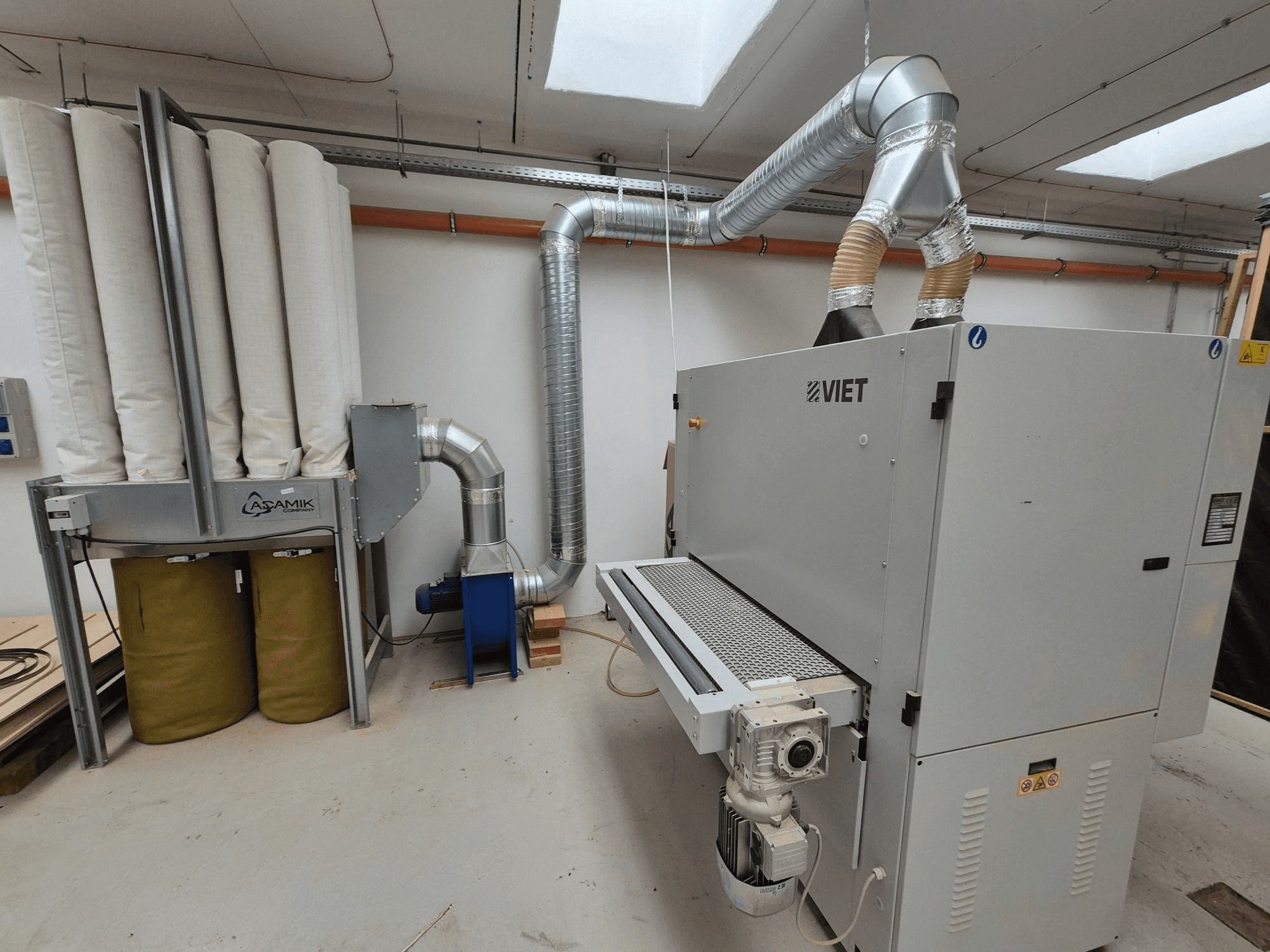 Viet dammutsugningssystem med cylindriska filter och ett silverfärgat utblås, sett framifrån i en verkstadsmiljö.