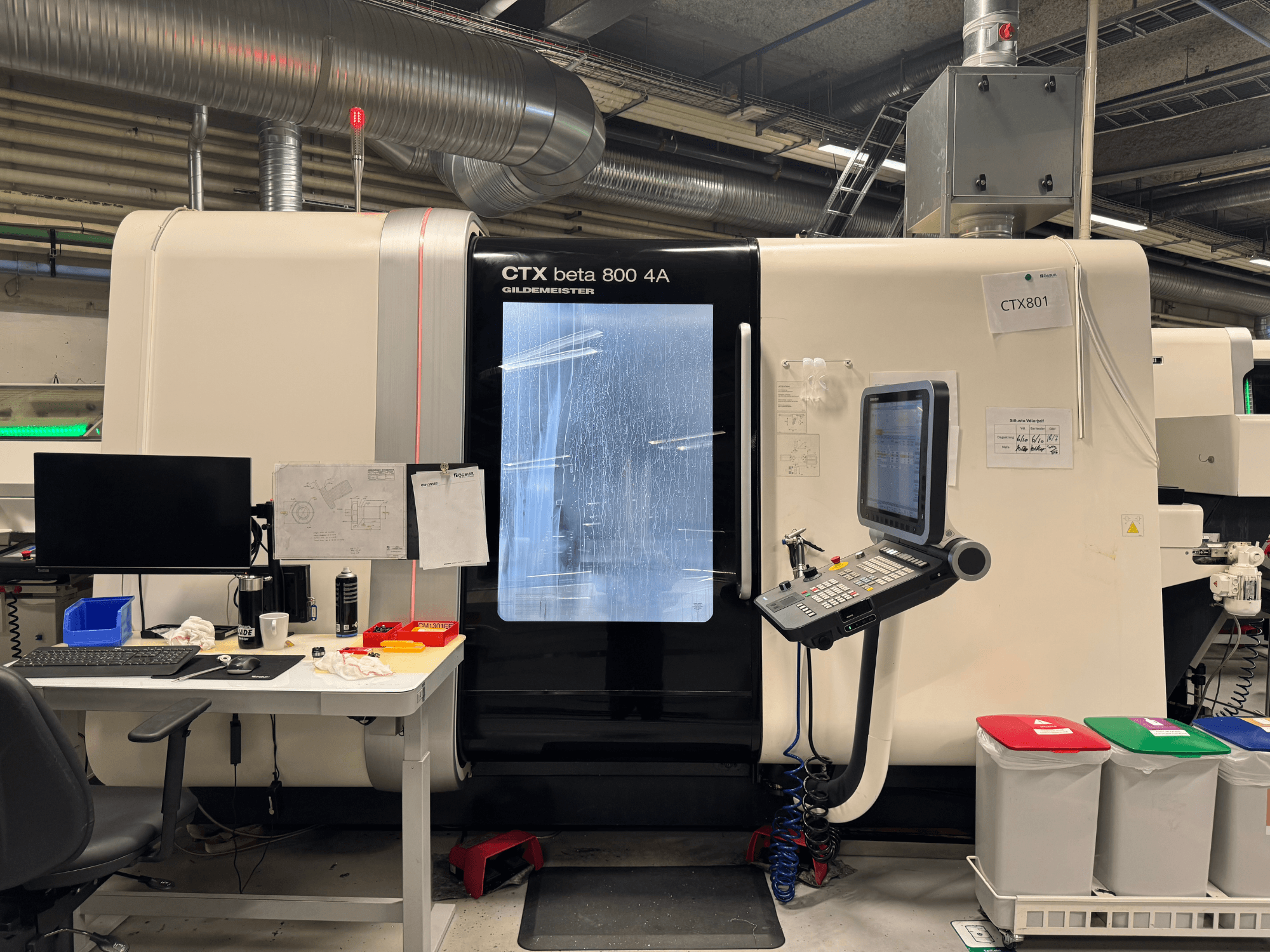 CTX beta 800 4A-maskin med kontrollpanel och bildskärm, vy från sidan, i en verkstad med kontorsinredning och färgade papperskorgar.