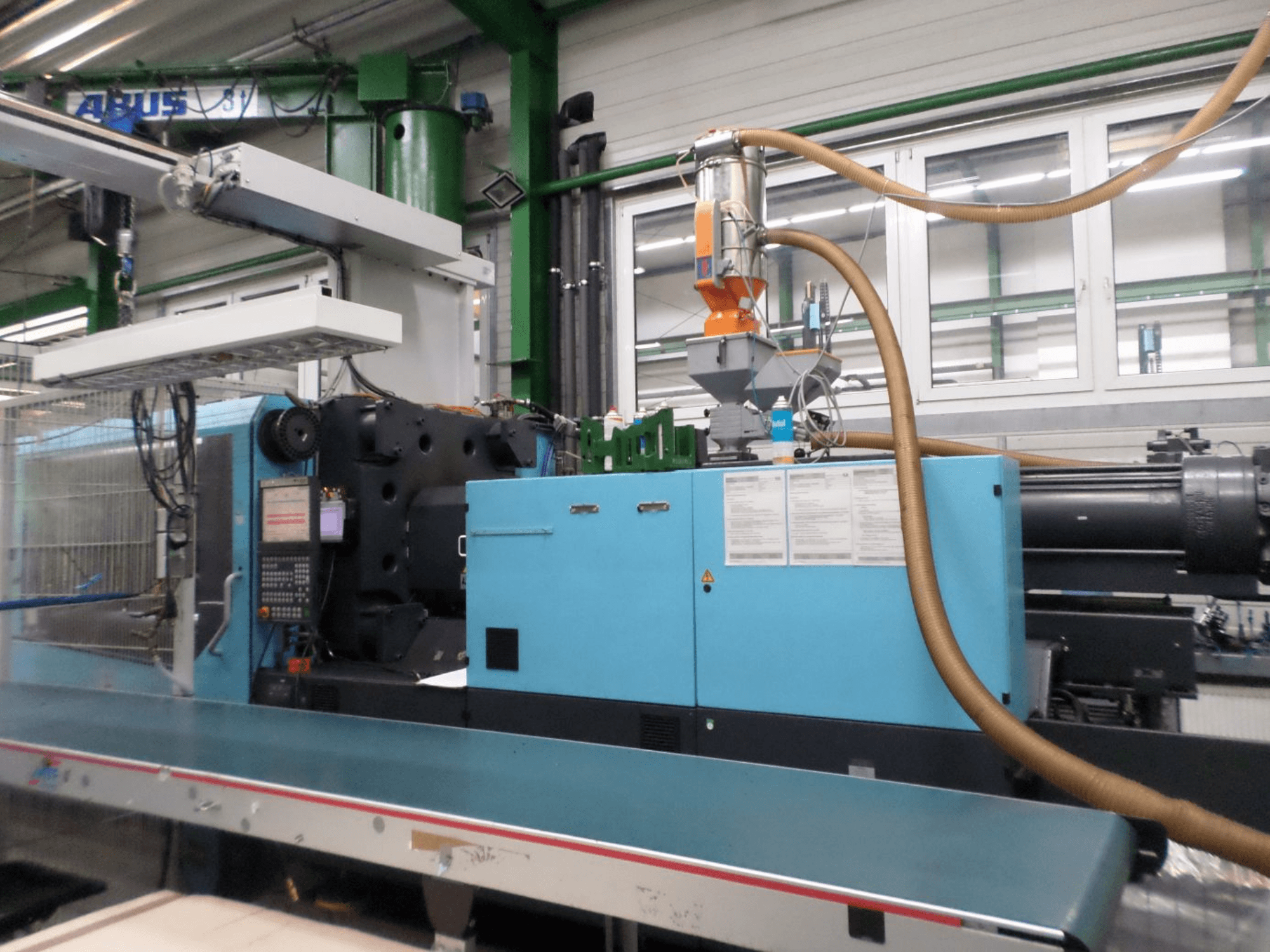 Framifrån sett på en hydraulisk formsprutningsmaskin av typen DEMAG D 420, där man ser kontrollpanelen, påfyllningstratten och de hydrauliska komponenterna.