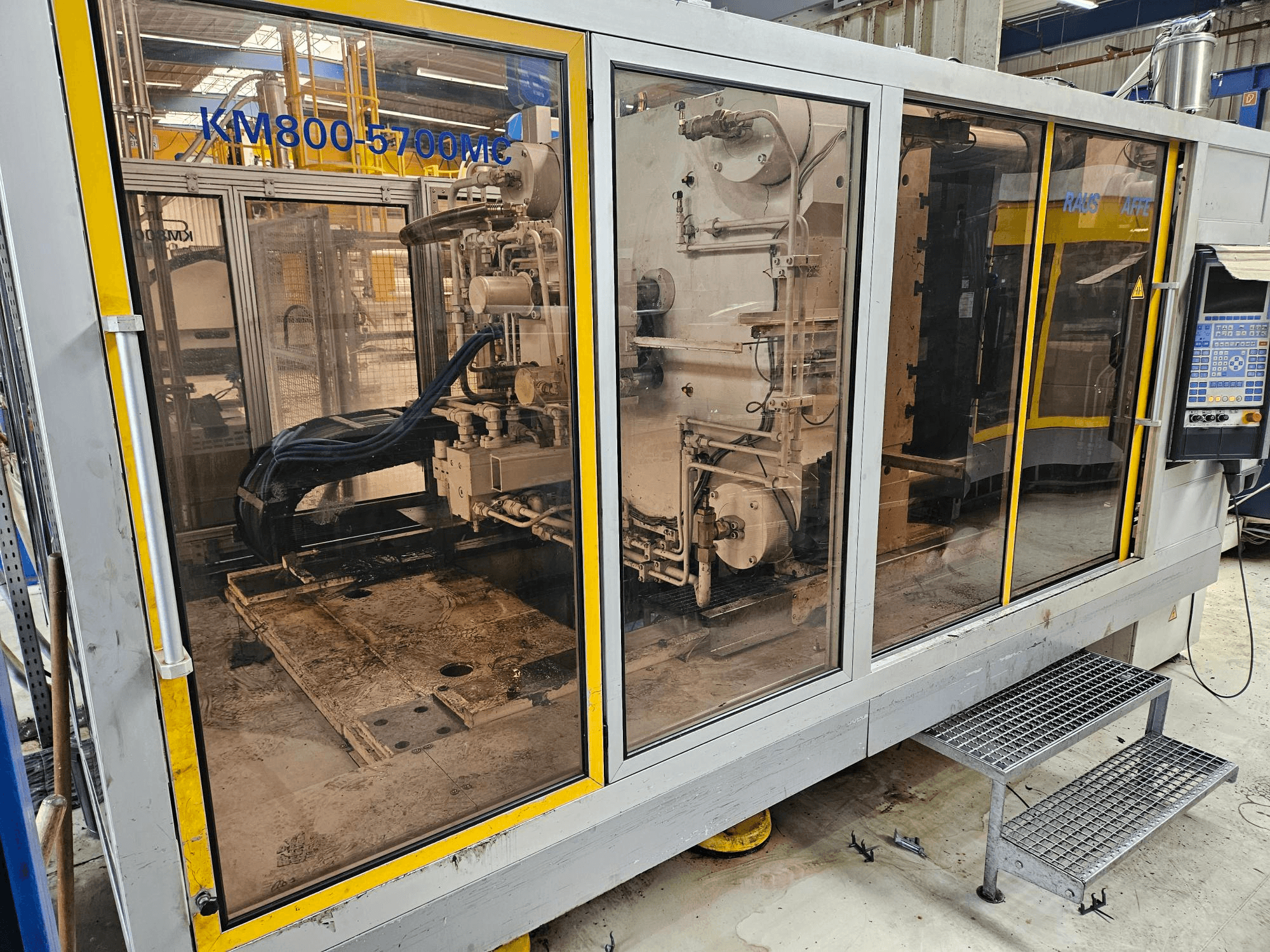 Hydraulisk formsprutningsmaskin Krauss Maffei KM800-5700 MC, framifrån sett med komponenterna synliga genom glaspanelerna.