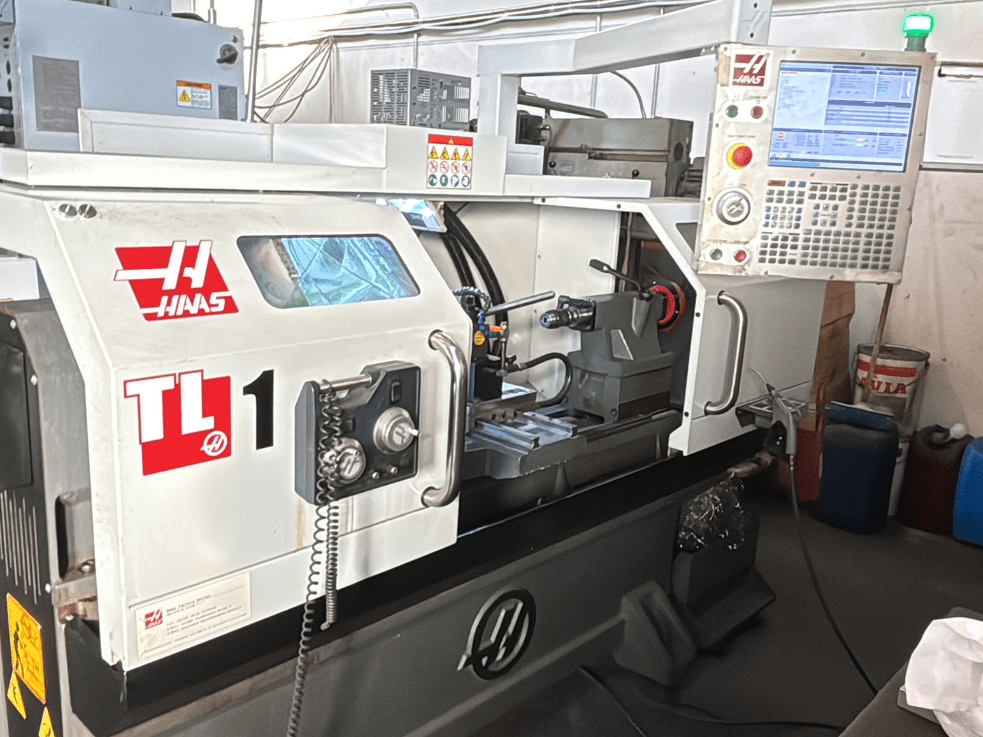 Haas TL-1 CNC-svarvmaskin, framifrån, har kontrollpanel med display, verktygshållare och säkerhetsetiketter.