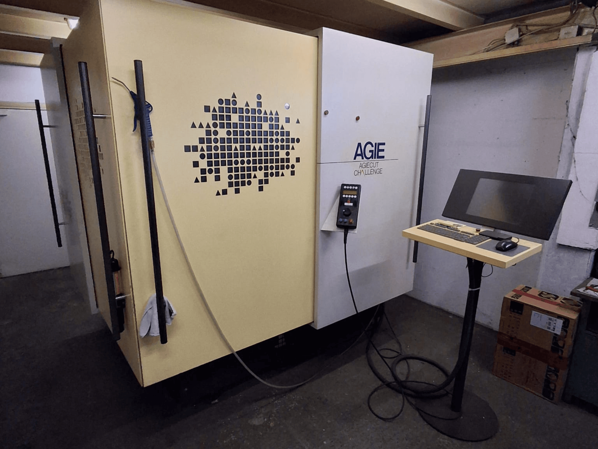 AGIE Agiecut Challenge, en 2-tråds-EDM-maskin i en verkstad, med kontrollpanel och bildskärm på ett stativ, sett framifrån.