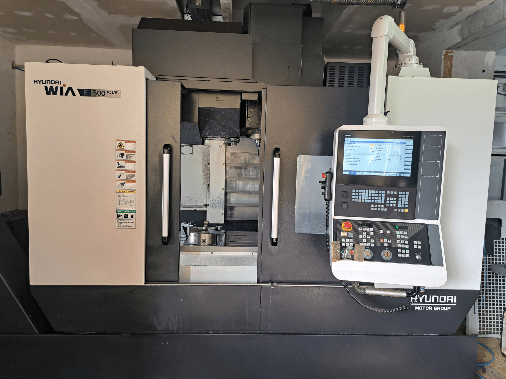 Hyundai WIA F500 Plus CNC-maskin framifrån, med digital kontrollpanel och säkerhetsetiketter.