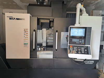 Hyundai WIA F500 Plus CNC-maskin framifrån, med digital kontrollpanel och säkerhetsetiketter.