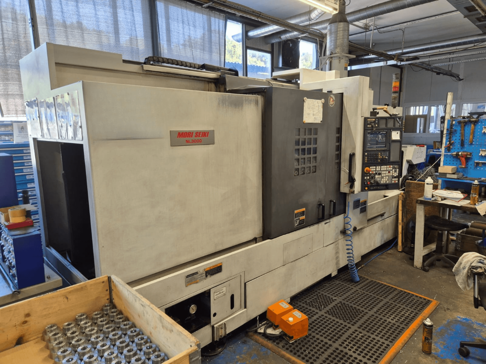 Mori Seiki NL3000 CNC-svarv i en verkstad, sidovy som visar kontrollpanel, verktyg och metalldelar i en trälåda.