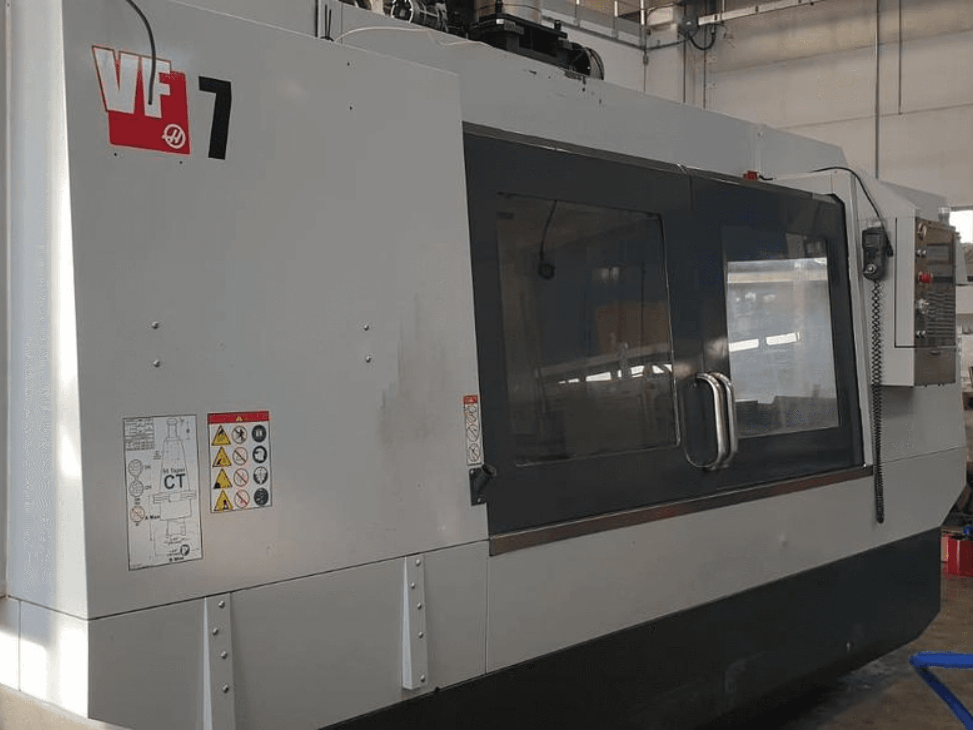 Haas VF-7 CNC-maskin i sidovy, med metallgrå finish, kontrollpanel och säkerhetsetiketter.