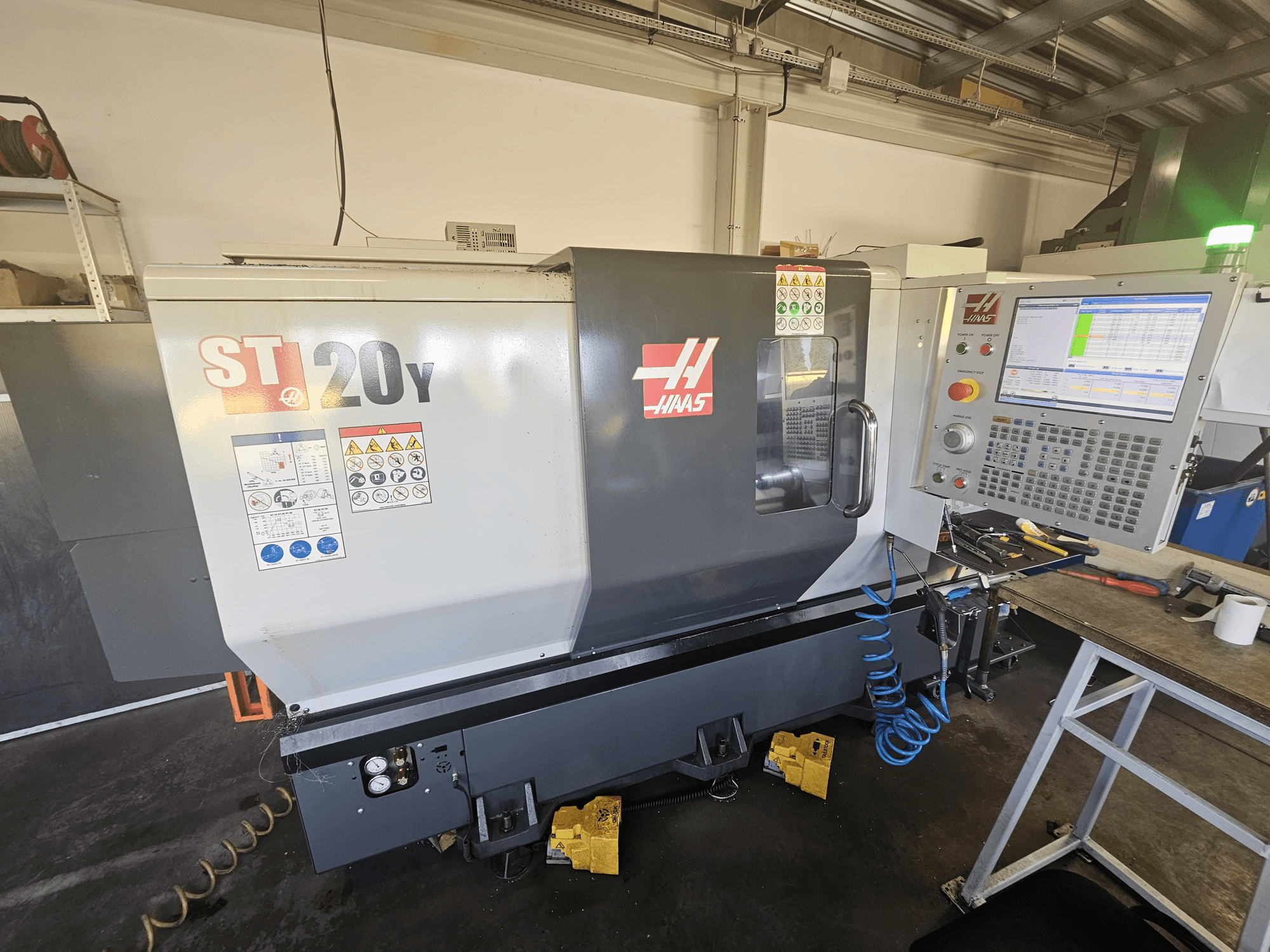 Haas ST-20Y CNC-svarv framifrån med kontrollpanel; inkluderar säkerhetsetiketter och luftslangdetaljer på sidan.