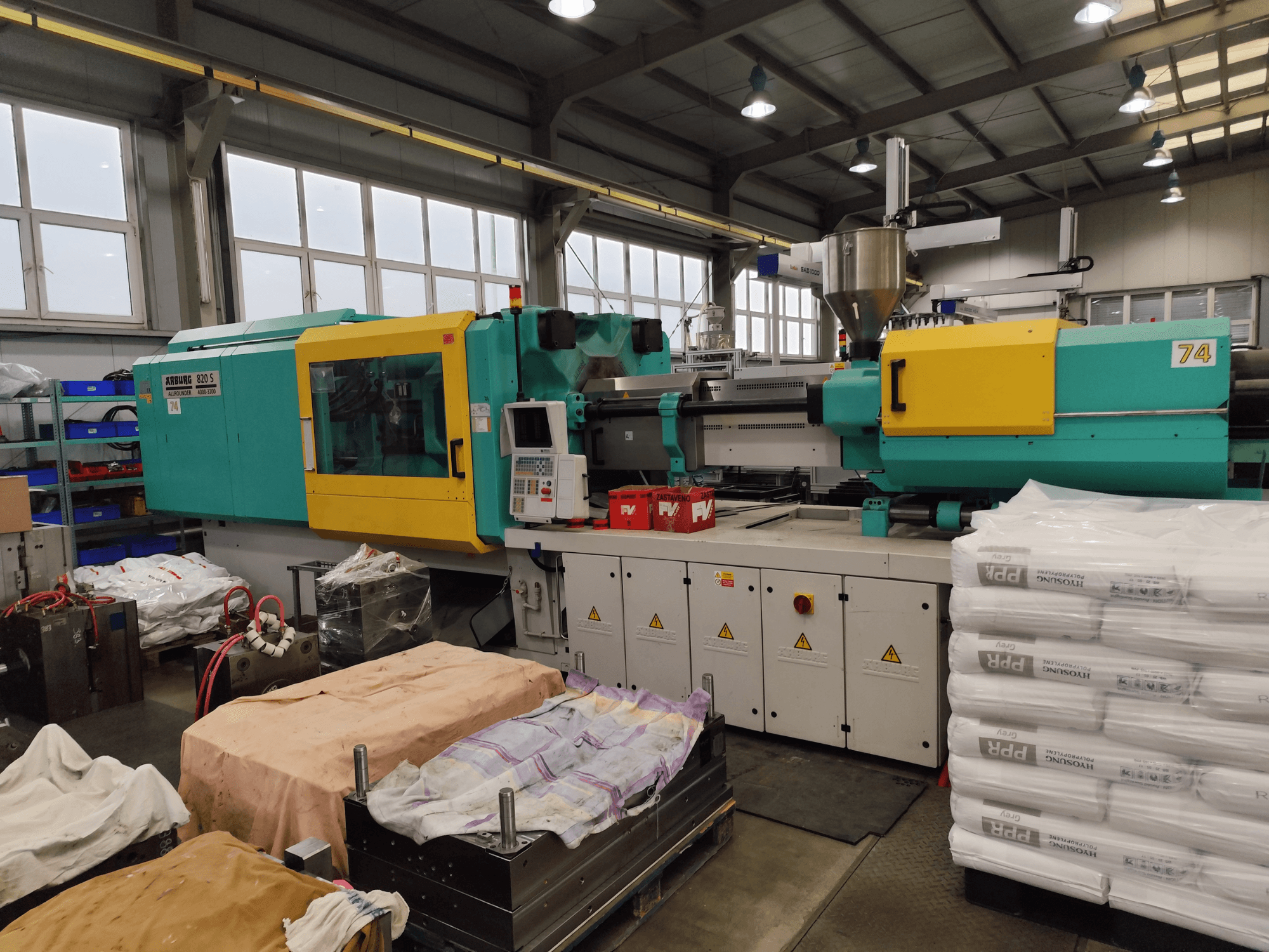Formsprutningsmaskin från Arburg, framifrån, teal- och gulfärgad exteriör, med verktyg och material i närheten.