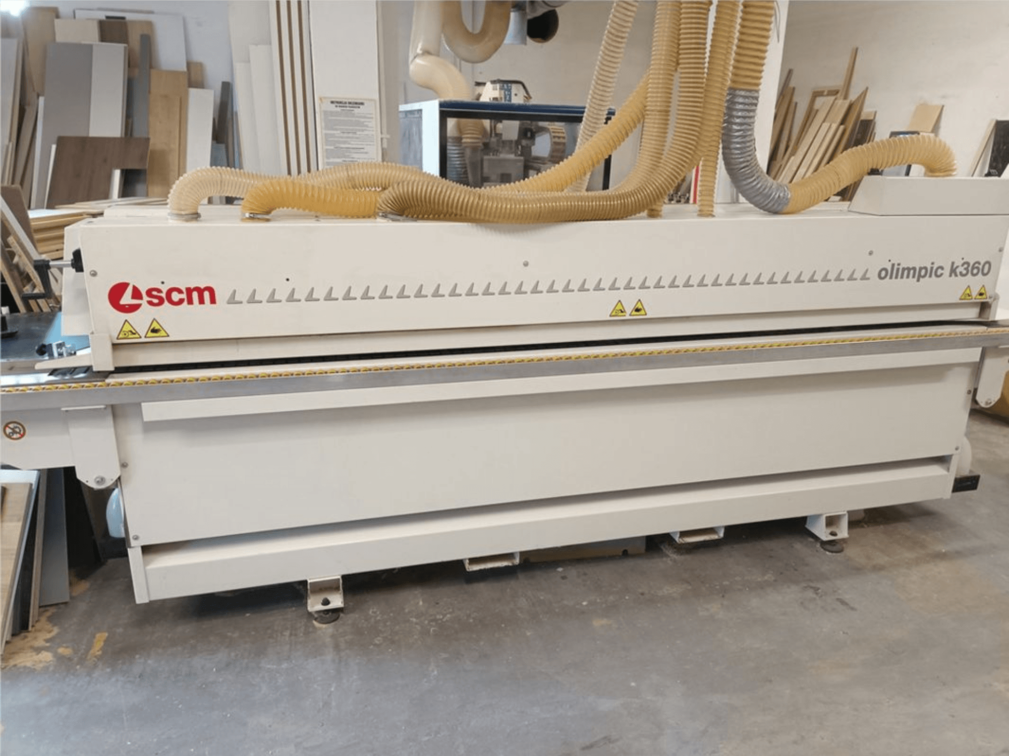 En SCM Olimpic K360 T-ER1 kantlistmaskin i en verkstad, framifrån sett med dammutsugsslangar och varningsetiketter.