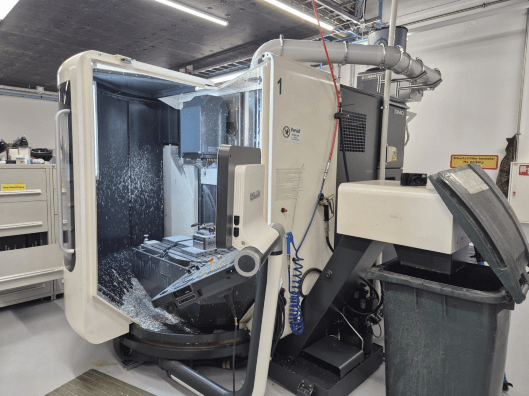 Öppen DMG-fräsmaskin med kylvätskespray, metallspån och verktygsreglage, sedd framifrån.