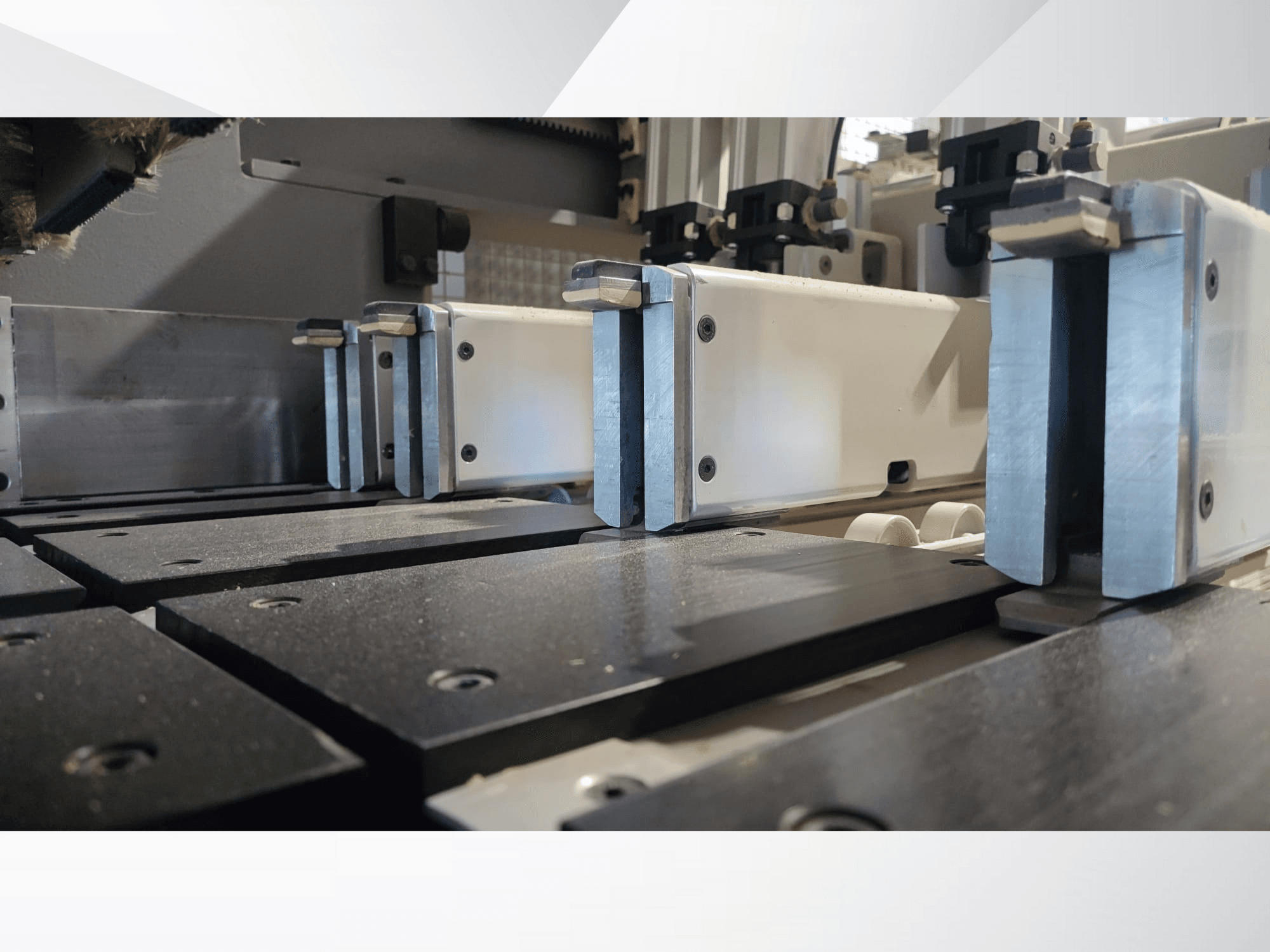 Närbild av en precisionsmaskins fastspänningsmekanism med metallbackar, svarta arbetsytor och synliga styrskenor.