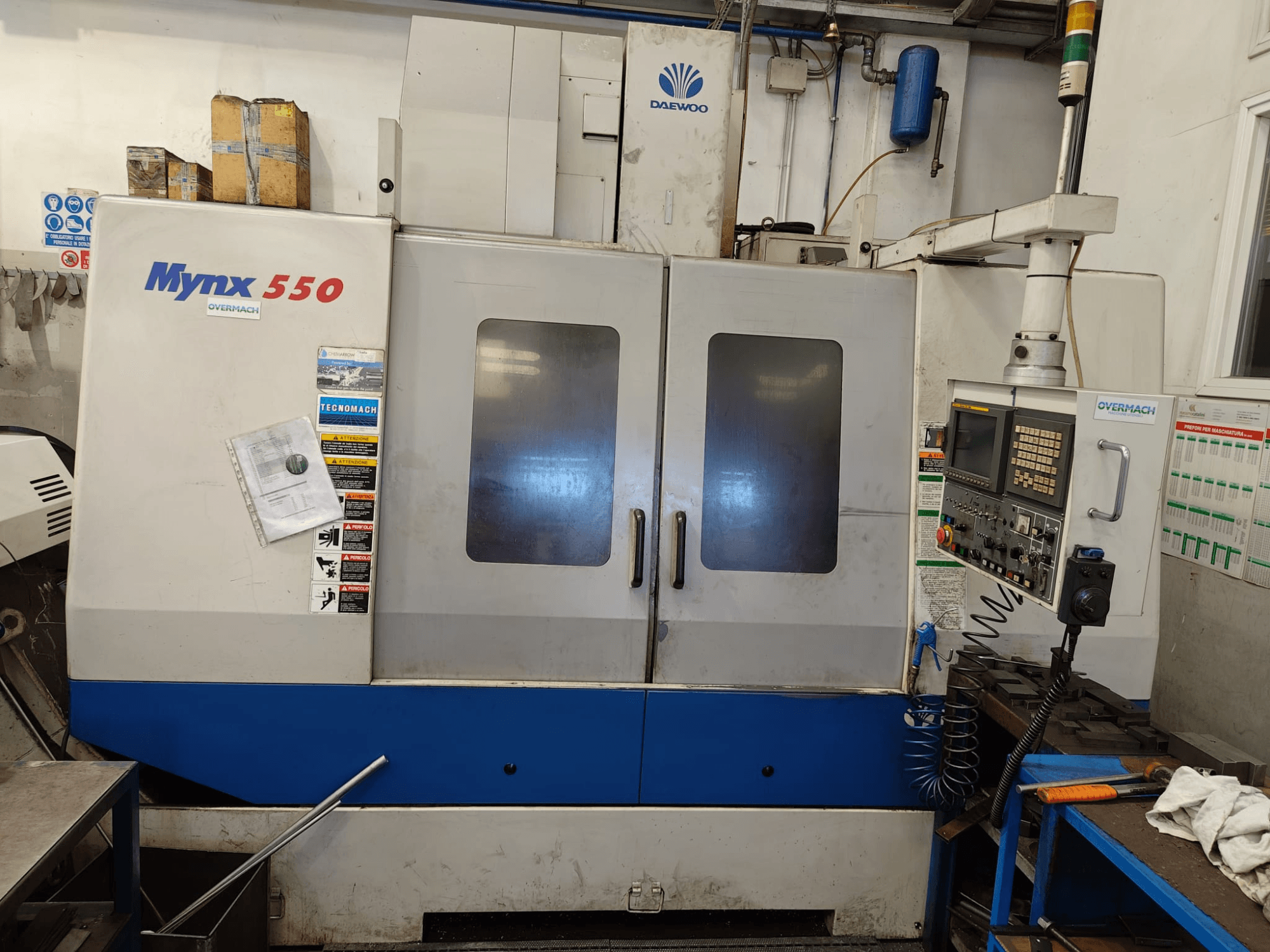 Vertikalt bearbetningscenter DAEWOO MYNX 550, framifrån, med kontrollpanel, två stora dörrar och säkerhetsetiketter.