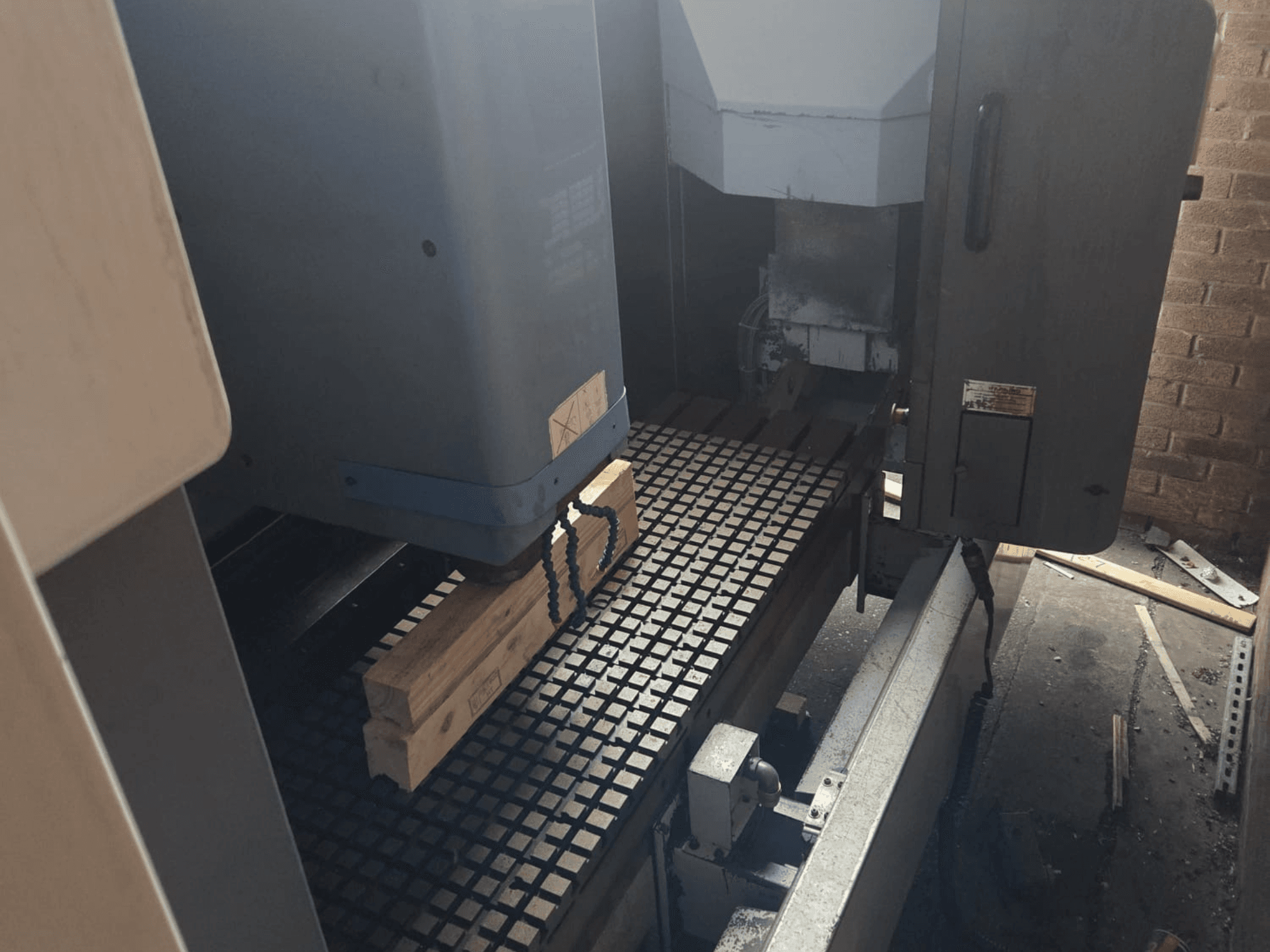 CNC-maskin framifrån med träplankor på ett rasterbord, med verktyg och reglage på sidan.