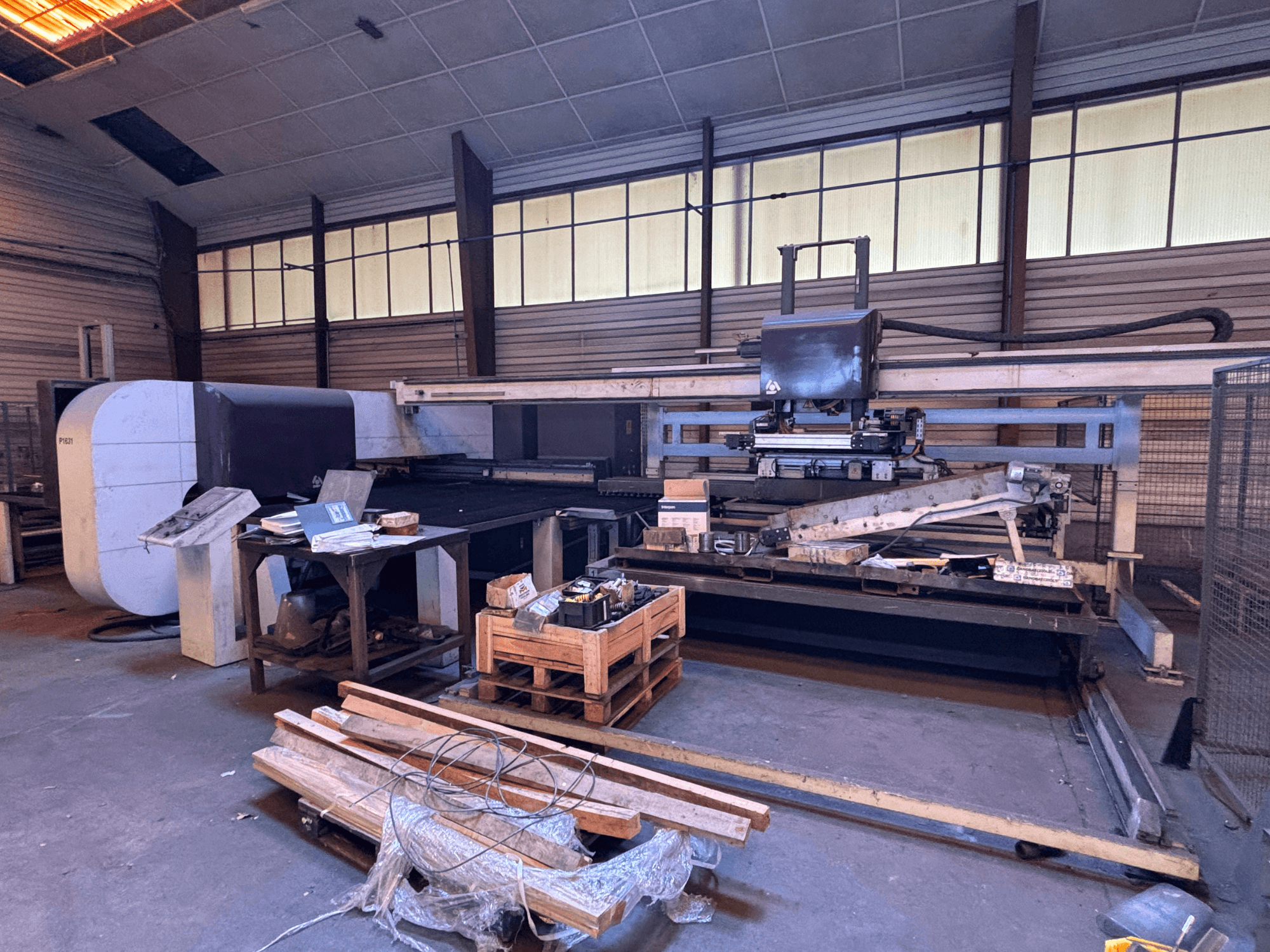 CNC-stansmaskin DANOBAT P1631 i en verkstad, vy framifrån, omgiven av material och verktyg på ett rörigt golv.