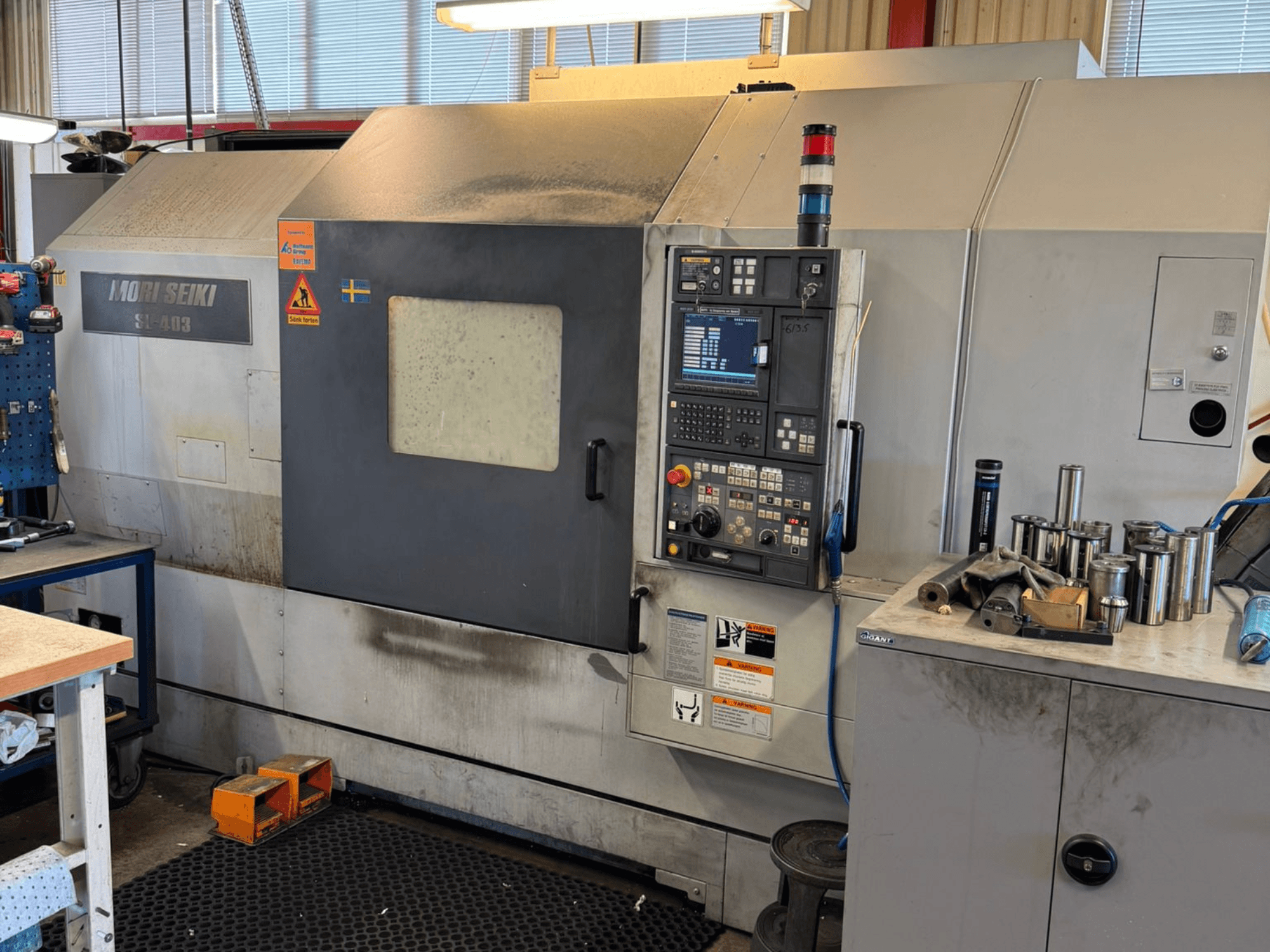 MORI SEIKI SL-403BMC/800 horisontell svarv i en verkstad, med kontrollpanel och närliggande verktyg, vy från sidan.