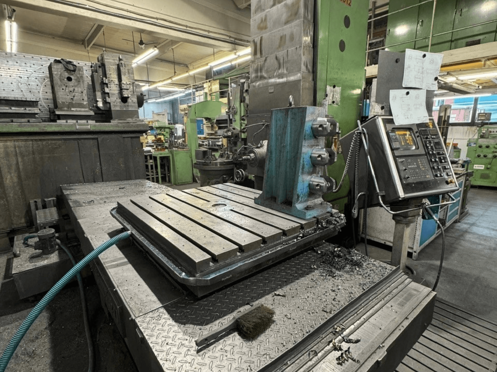 En JUARISTI 12/TS1.7-borrmaskin i en verkstad, sett från sidan, där man ser ett metallbord med spår och en kontrollpanel i närheten.