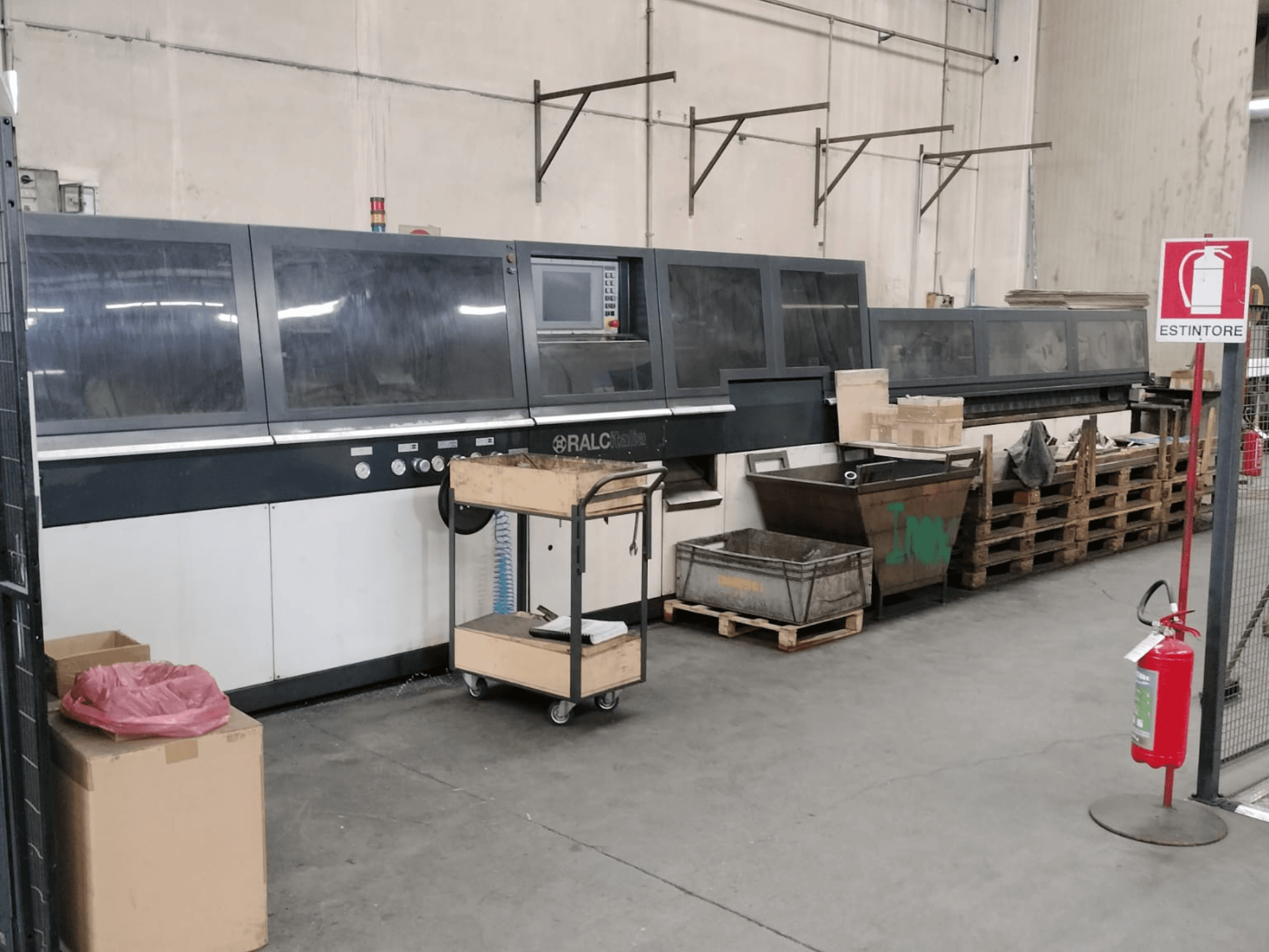 RALC industrimaskin i en fabriksmiljö, framifrån med synlig kontrollpanel; träpallar och brandsläckare i närheten.