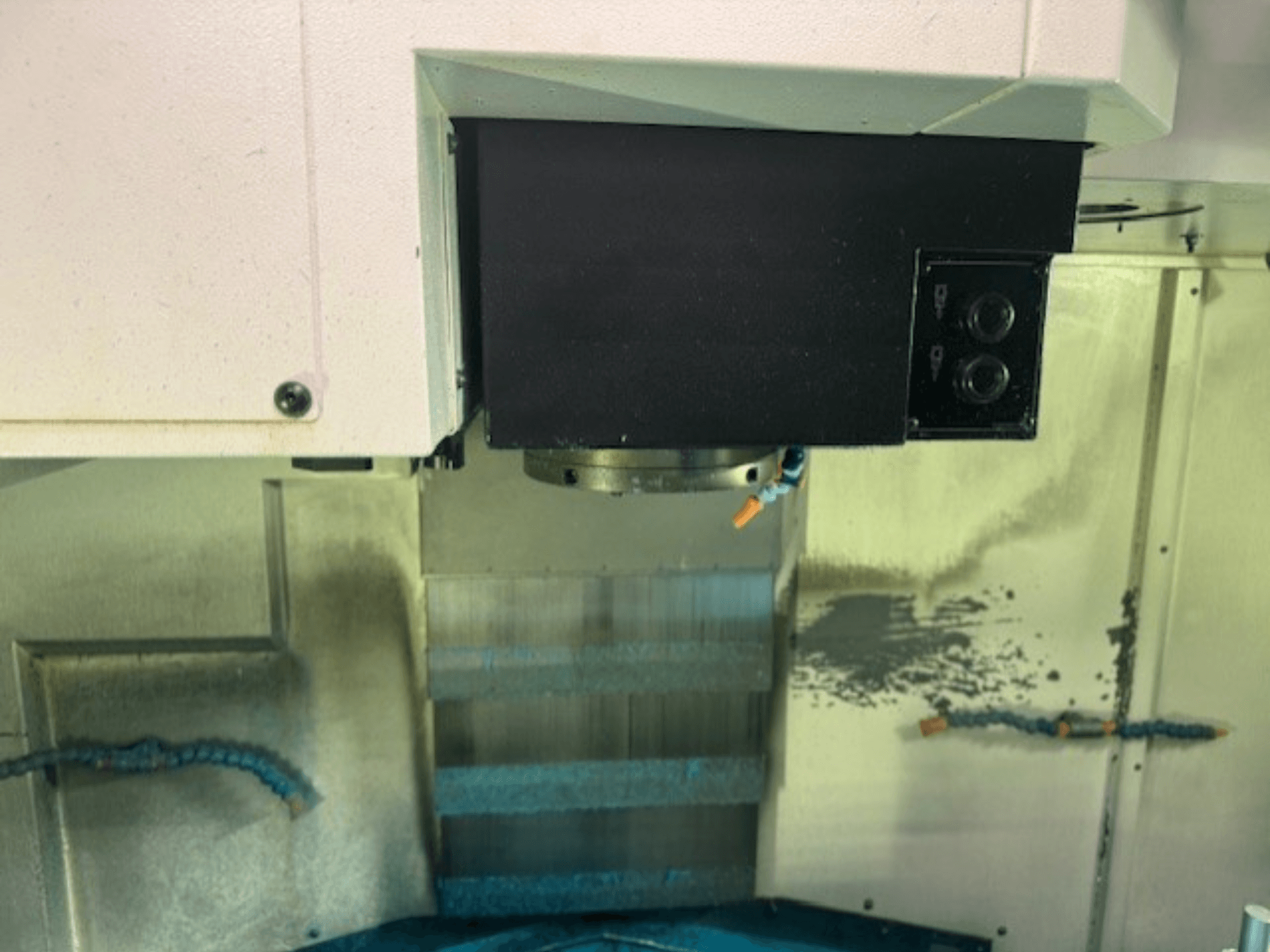 Närbild av en CNC-fräsmaskins kontrollpanel och verktygshållare, som visar varumärkesdetaljer, knappar och arbetsyta.