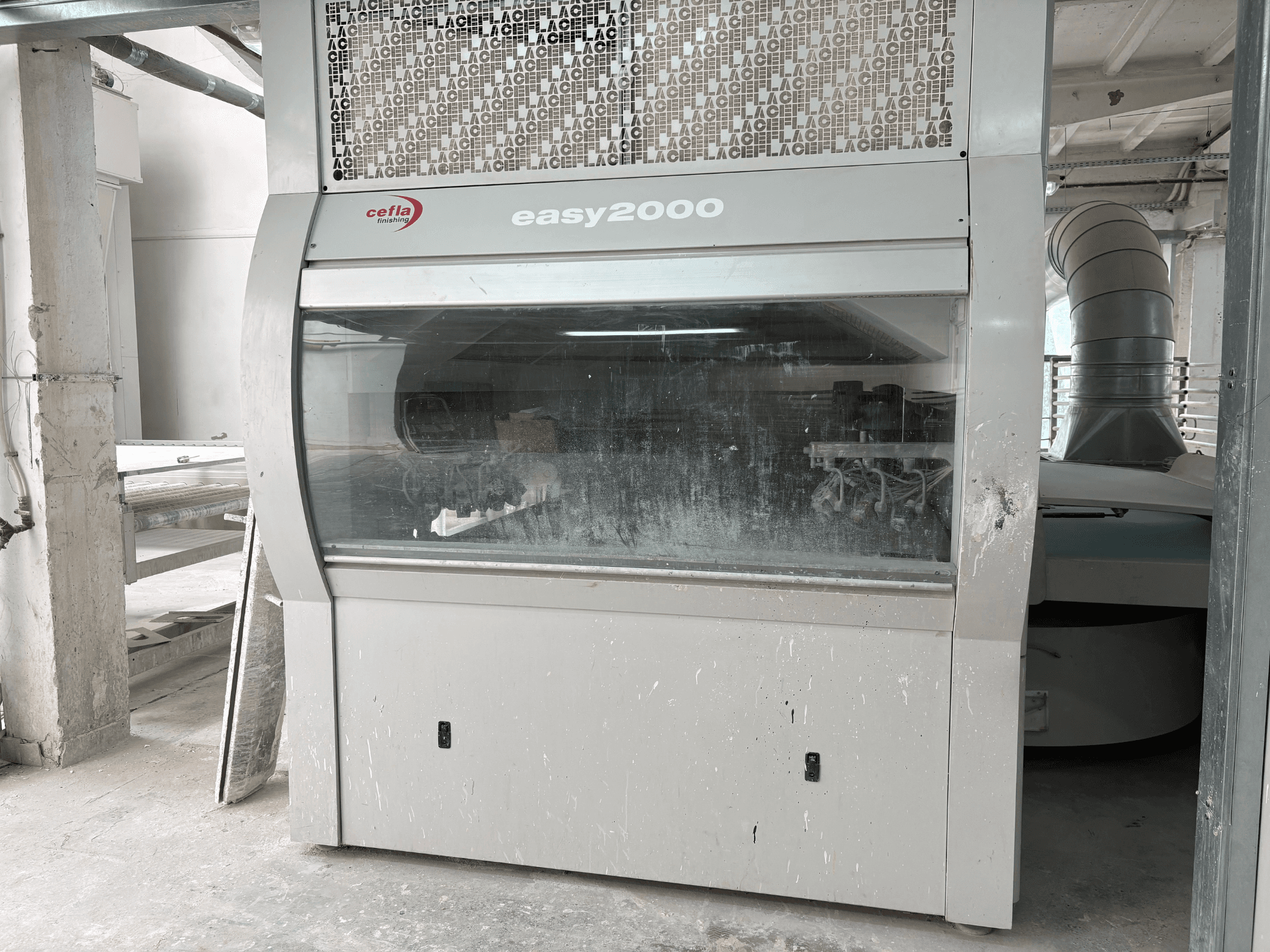 Cefla EASY 2000 D-maskinen sedd framifrån, med en stor genomskinlig panel, dammig yta och synliga inre komponenter.