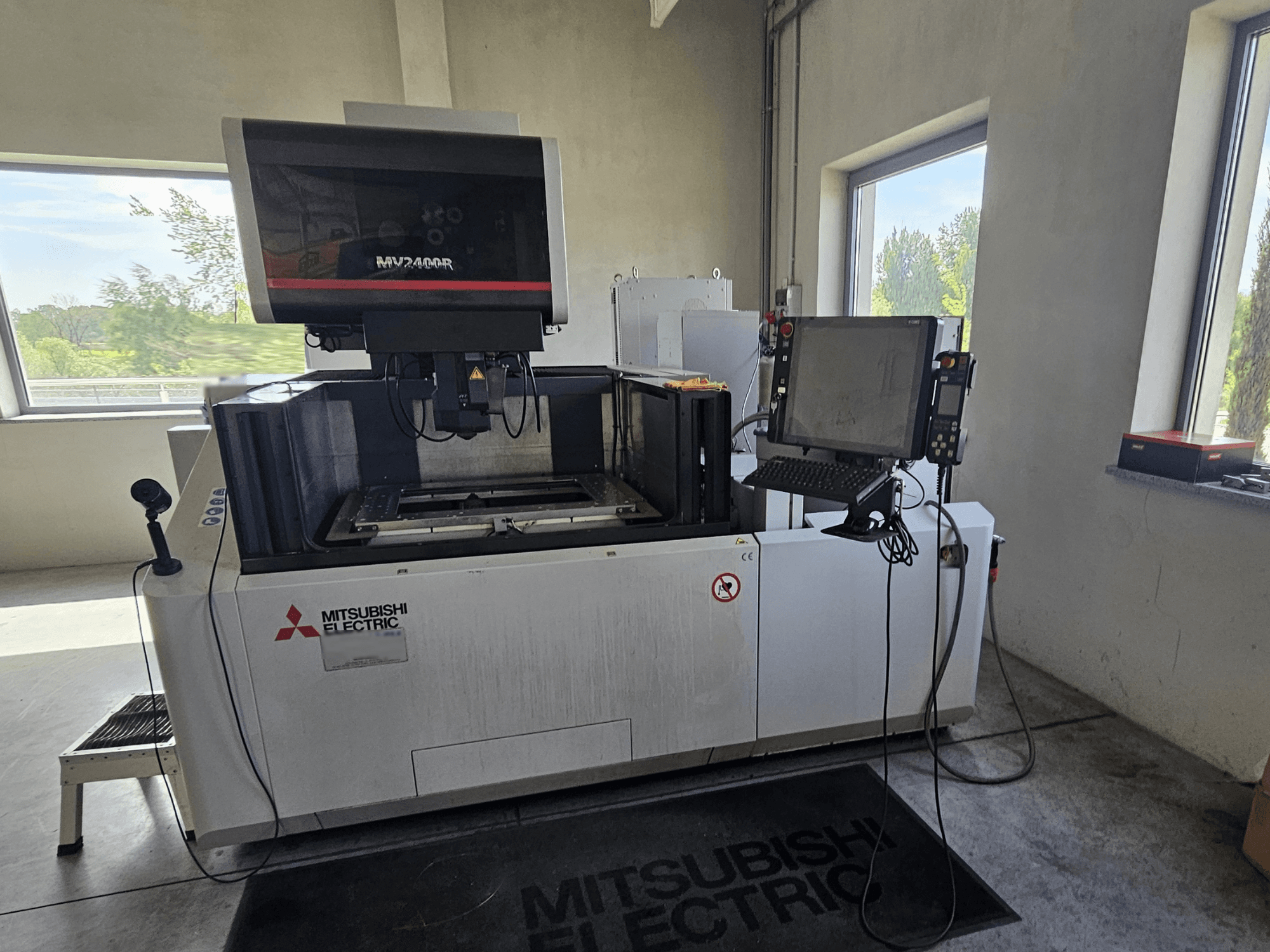 Mitsubishi MV2400R Wire EDM-maskin i en verkstad, med kontrollpanel med pekskärm och arbetsyta.