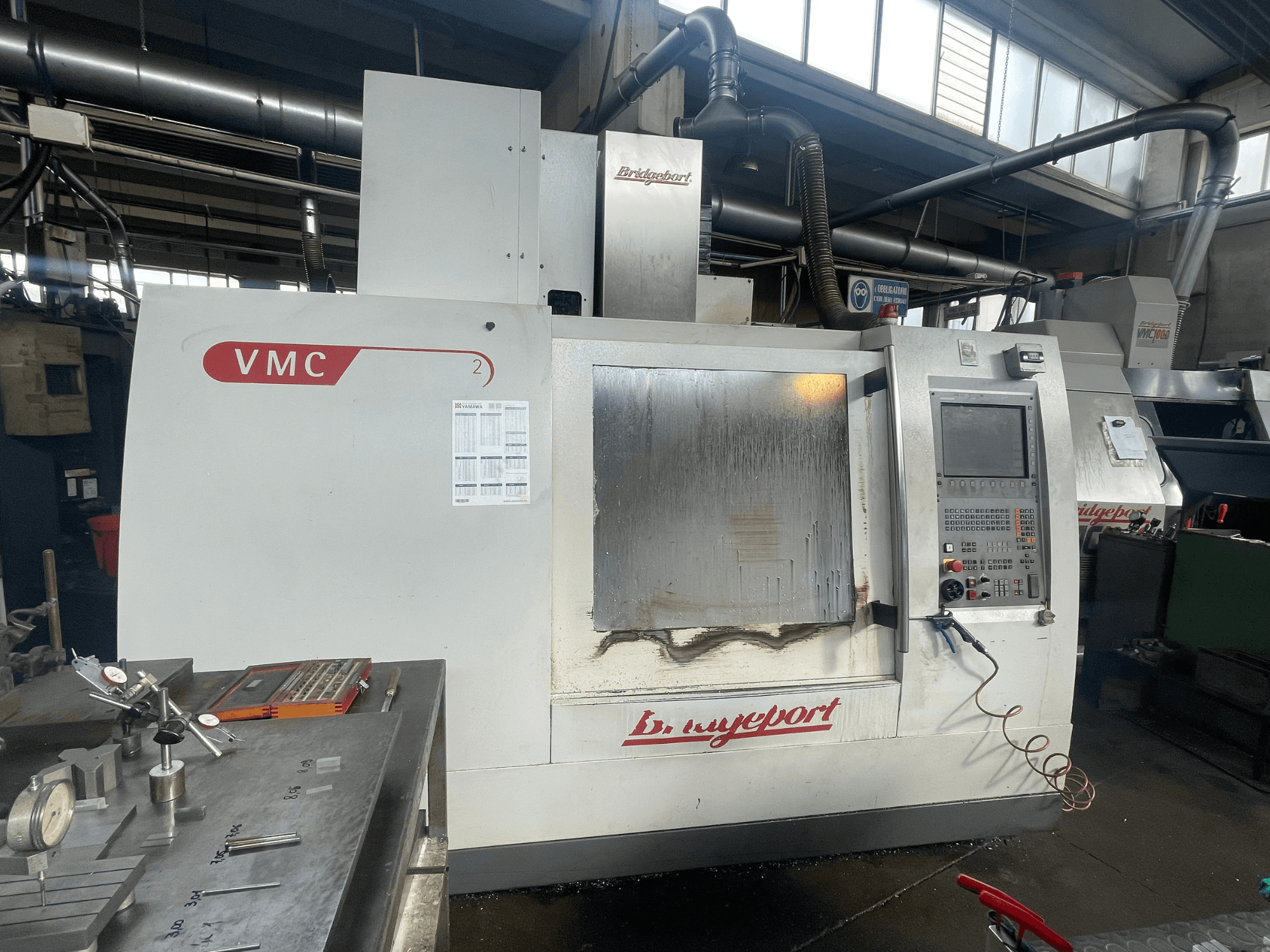 Vertikalt bearbetningscenter av typen Bridgeport VCM 800-30 i en verkstad, med kontrollpanel och verktygsbord. Framifrån med synliga detaljer.