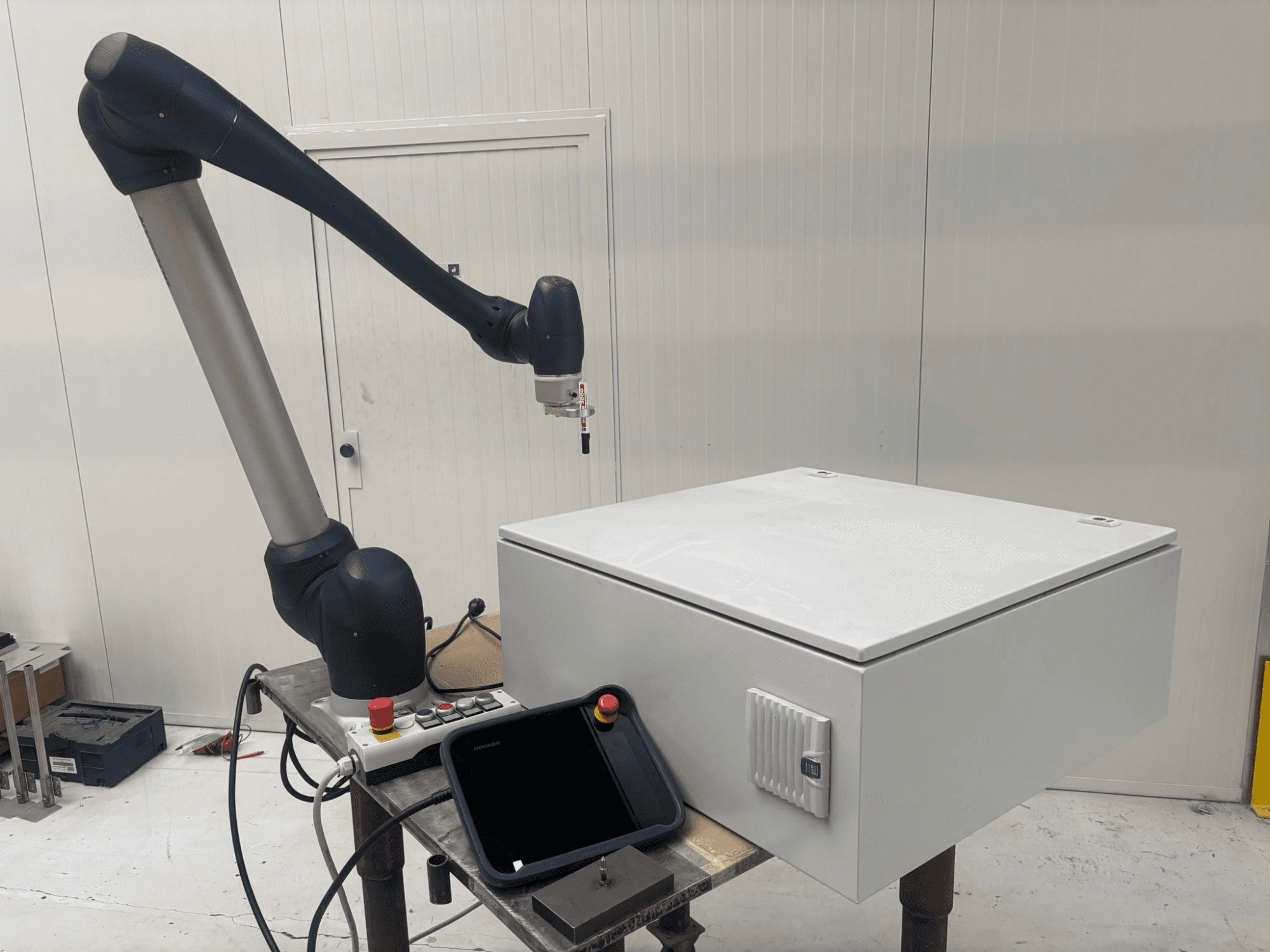 DOOSAN M0617 kollaborativ robot i sidovy, med robotarmen utsträckt över ett kontrollgränssnitt och en vit låda på ett bord.