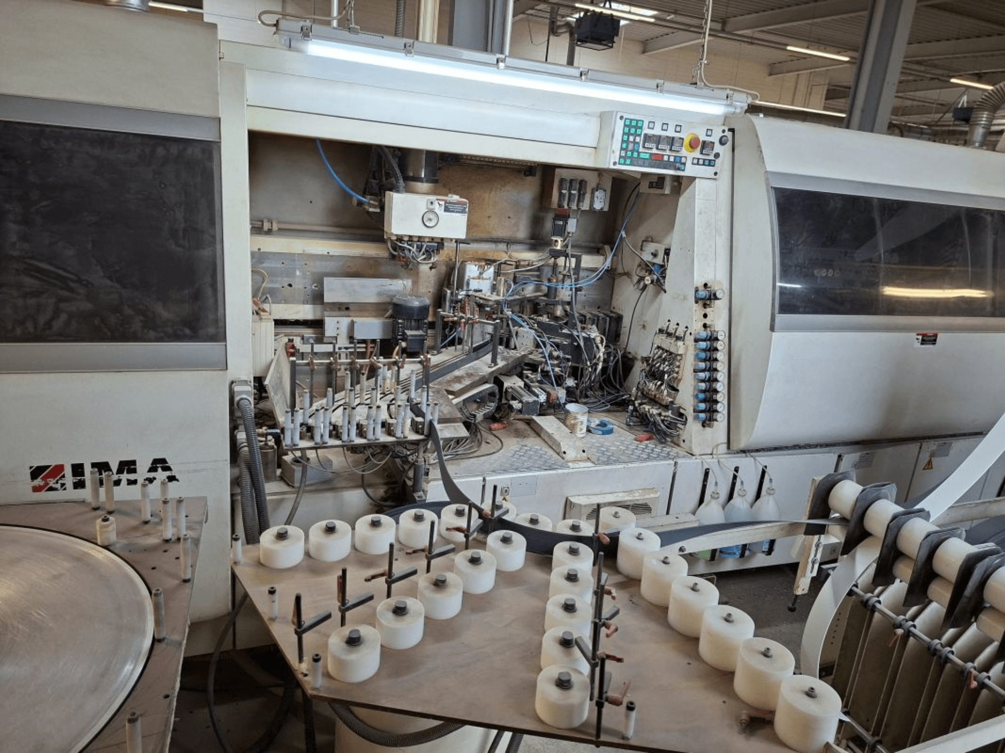 IMA:s maskinpark sedd från sidan, med komplexa mekaniska komponenter och ett runt bord med vita spolar.