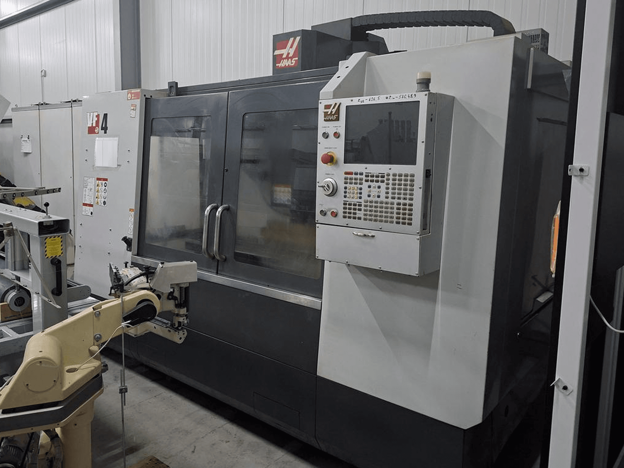Haas VF-4 CNC-fräsmaskin framifrån, med en numerisk styrpanel och robotarm för automatisering.