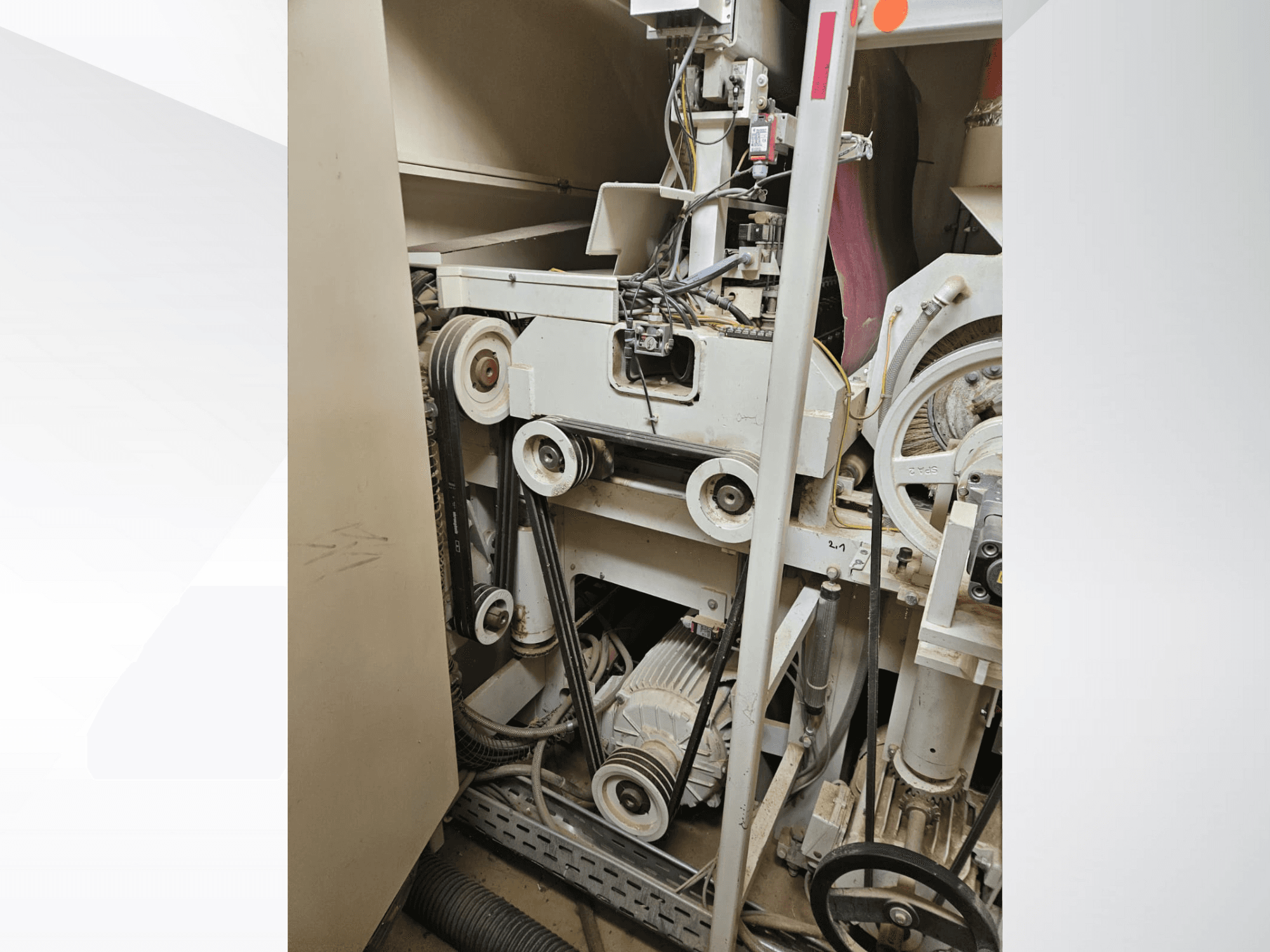 Inredning till industrimaskin med remmar och remskivor, med motor och kablage, sedd från sidan.