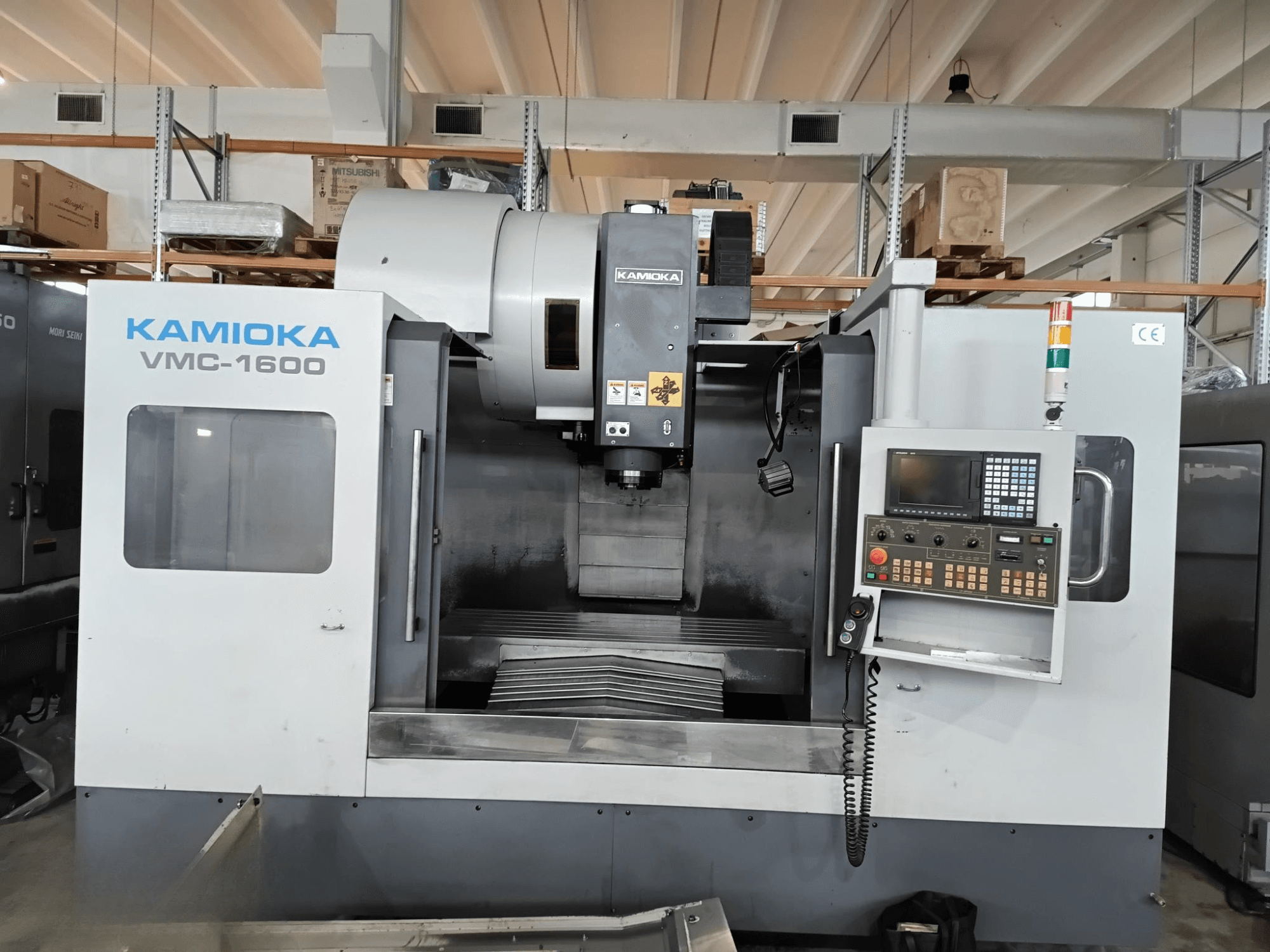 Kamioka VMC-1600 vertikal fleroperationsmaskin i fabriksmiljö, framifrån med kontrollpanel och synlig bearbetningsbädd.